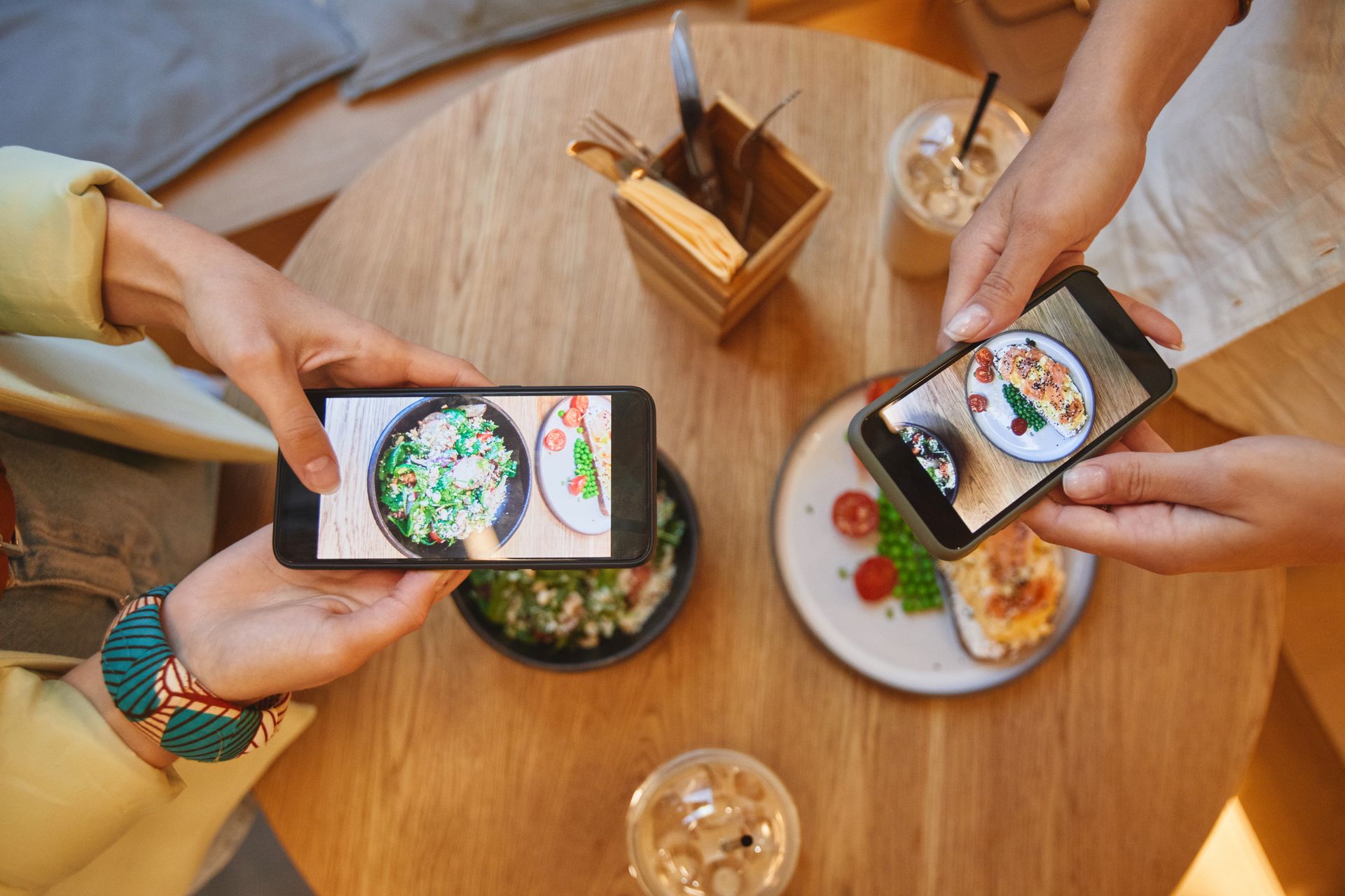 Two people photographing plates of food with their phones