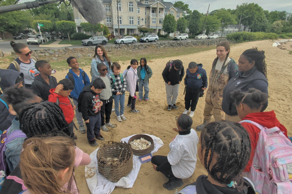 Students and educators gathered around historic oyster baskets during a Sandy Ground educational program