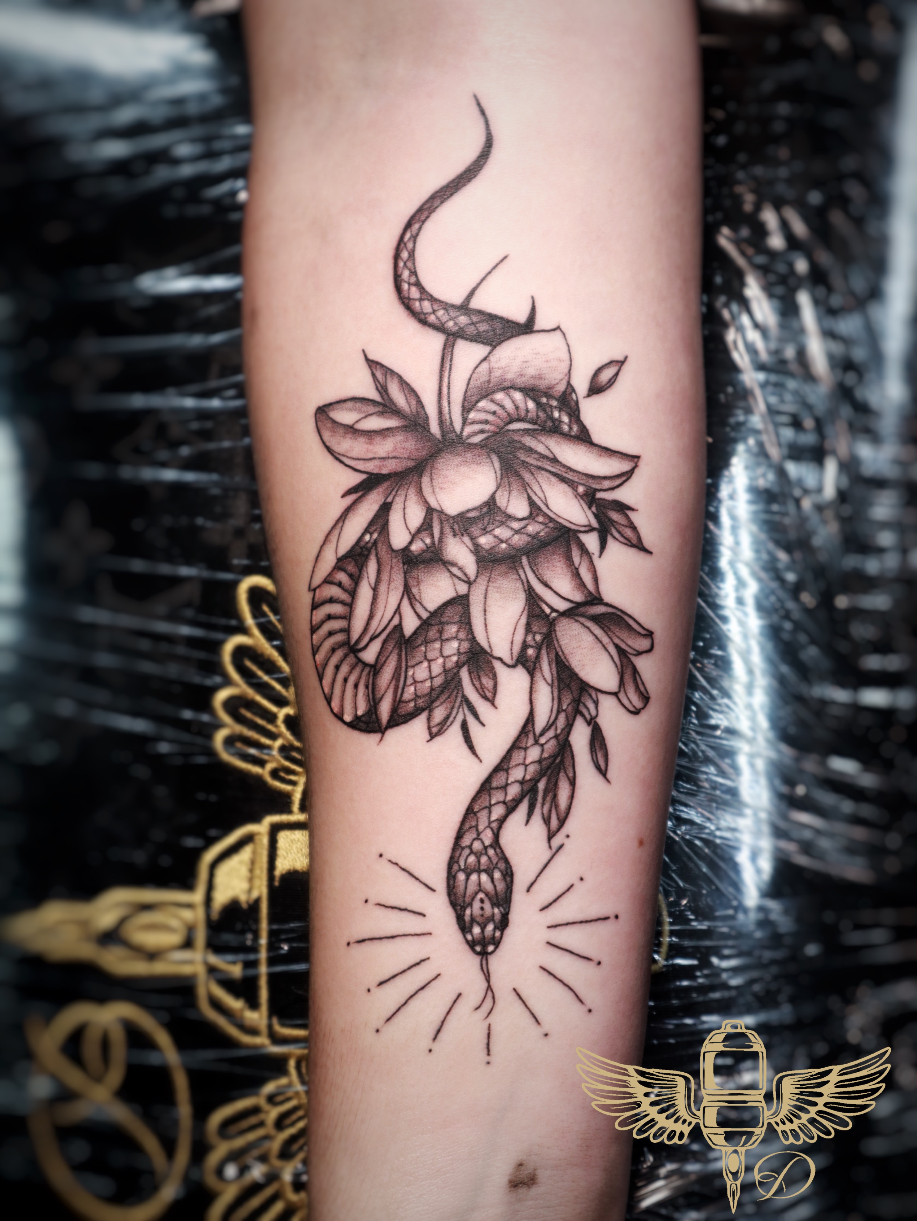 Tattoo of a snake intertwined with a lotus flower, featuring intricate black-and-grey detailing and radiating lines, showcasing Droe's neotraditional tattoo style at Game Face Tattoo.