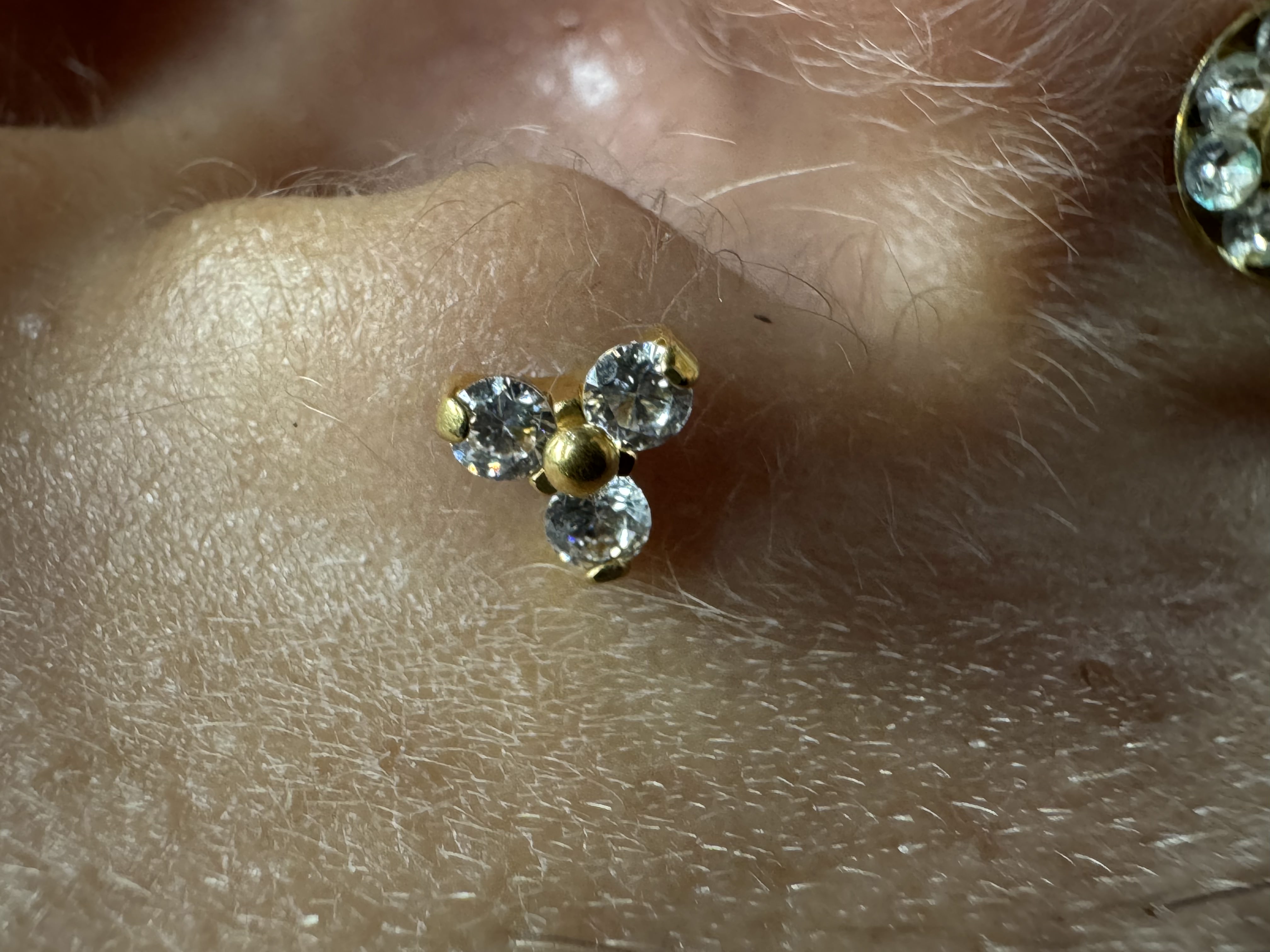 Close-up of a gold body piercing jewelry with three clear gemstones, showcasing intricate design and high-grade materials, emphasizing Mariano's expertise in body modifications at GameFace Tattoos.