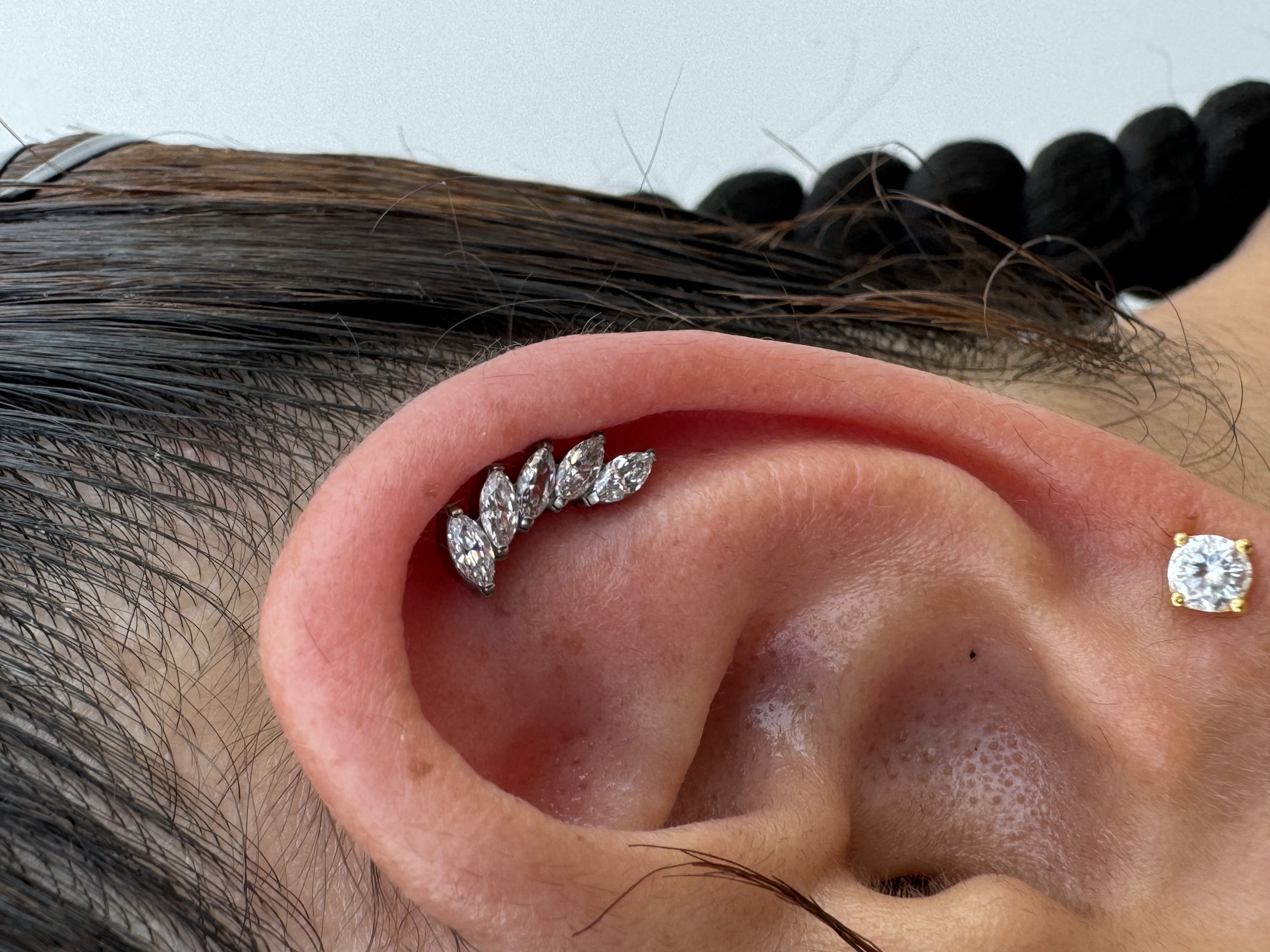 Close-up of a pierced ear showcasing a decorative ear cuff with multiple sparkling gemstones, alongside a stud earring, highlighting contemporary body modification aesthetics.