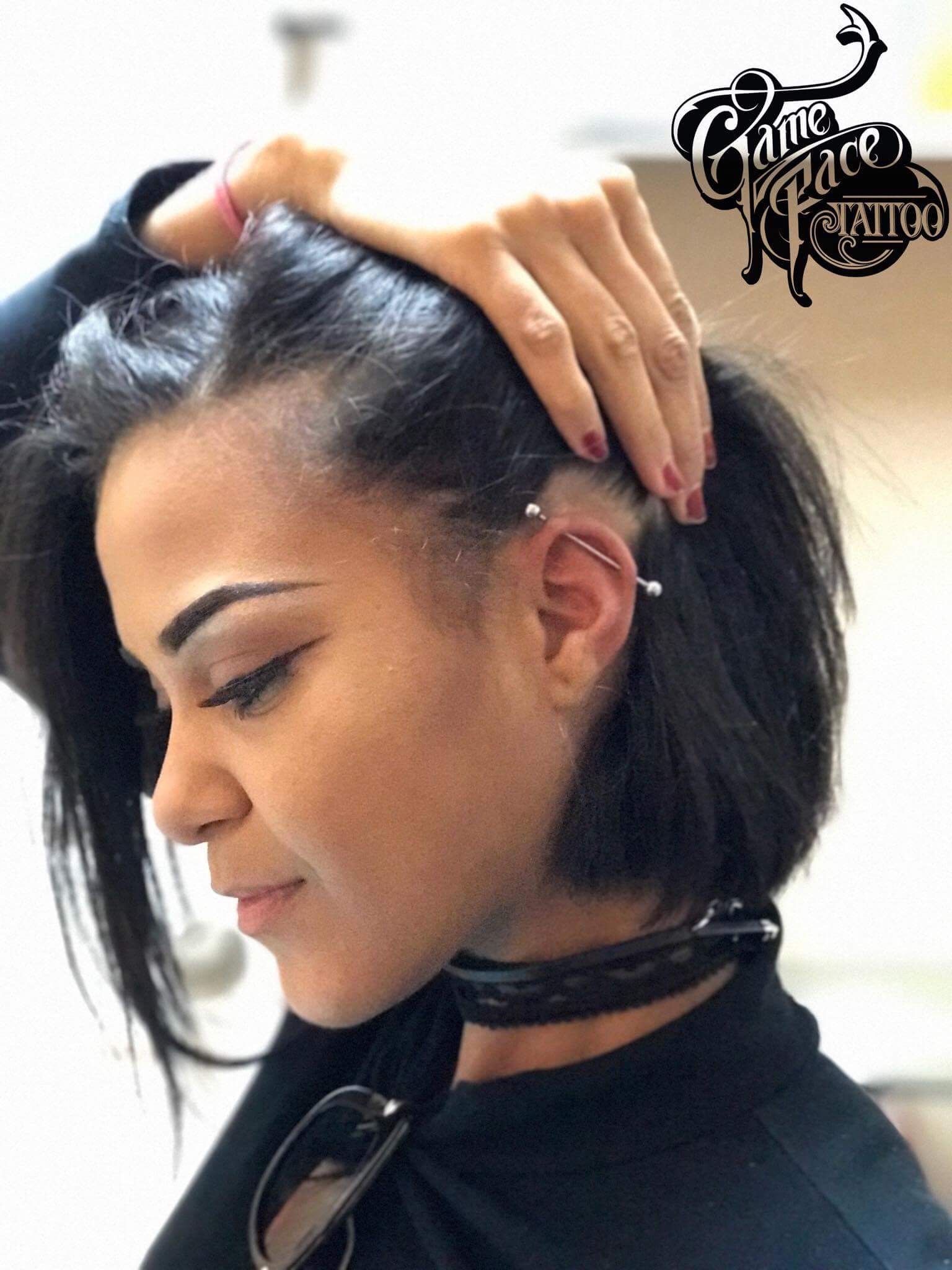Woman with short hair showcasing multiple ear piercings, wearing a black top and choker, with GameFace Tattoos logo in the corner.