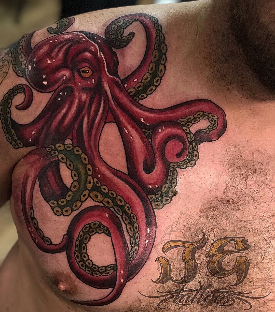 Octopus tattoo in vibrant red and green ink on a man's chest, showcasing intricate details and artistry by Jest Estevez at GameFace Tattoos.