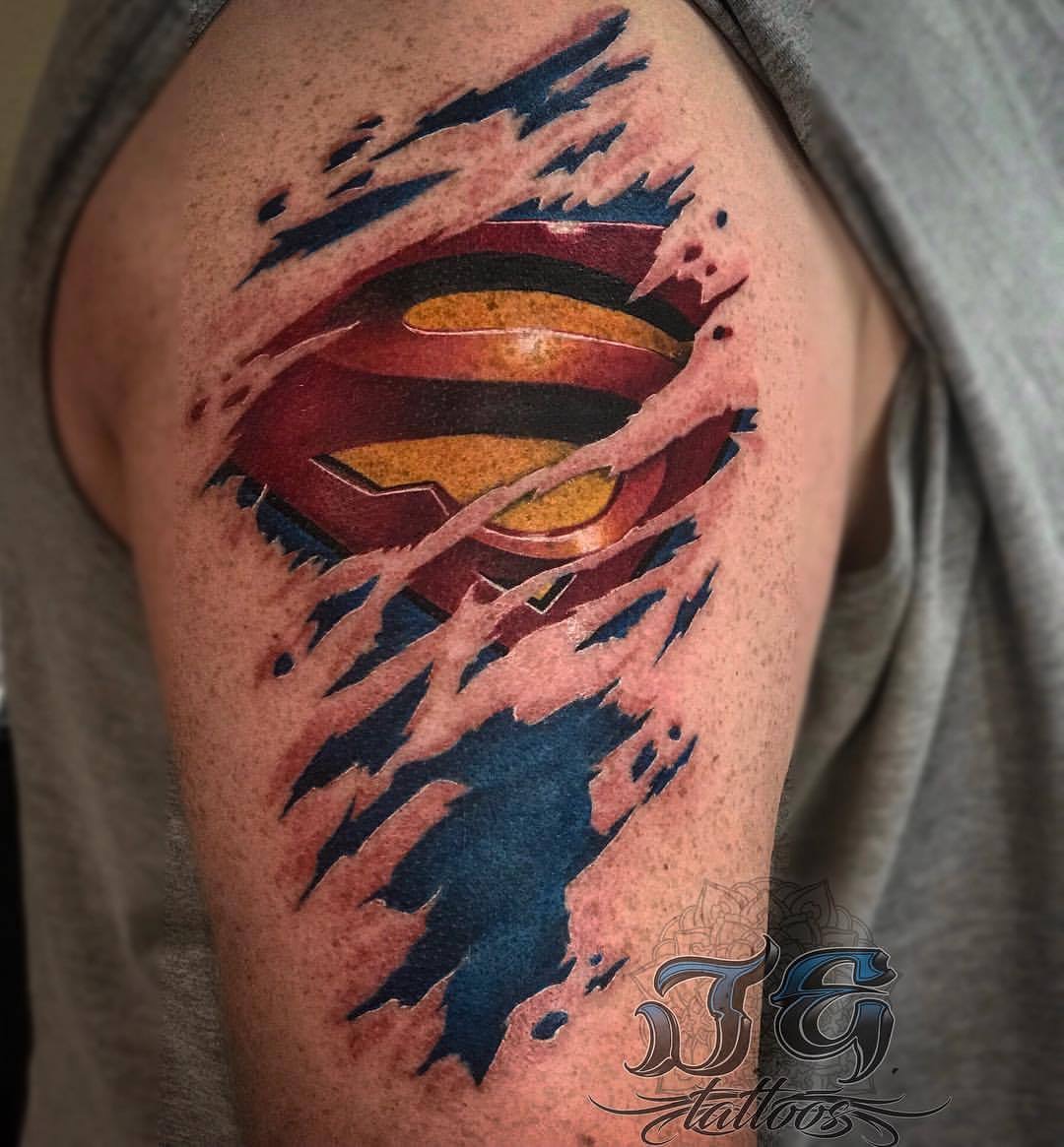 Tattoo of a Superman logo on a person's arm, showcasing vibrant colors and a 3D effect with torn skin design, representing Jest Estevez's artistry at GameFace Tattoos.