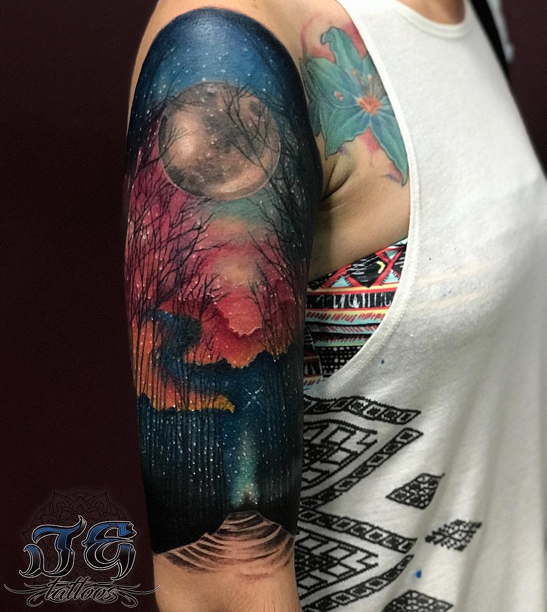 Colorful tattoo on arm featuring a night sky with a full moon, trees, and a galaxy, showcasing Jest Estevez's artistry at GameFace Tattoos.