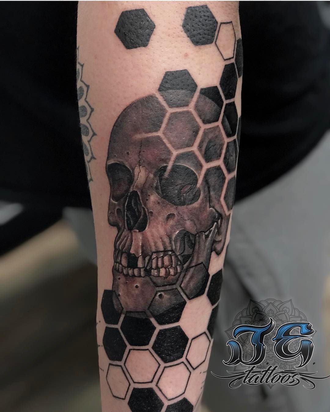 Black and gray tattoo of a skull surrounded by hexagonal patterns on a forearm, showcasing Jest Estevez's artistry at GameFace Tattoos.