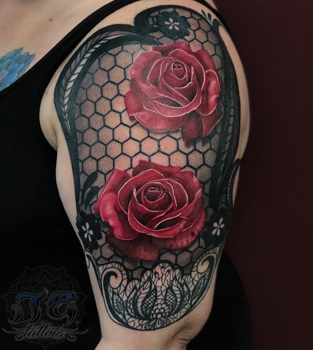Detailed tattoo featuring vibrant red roses on a shoulder, surrounded by intricate black lace and a honeycomb pattern, showcasing the artistry of Jest Estevez at GameFace Tattoos in Orlando, FL.