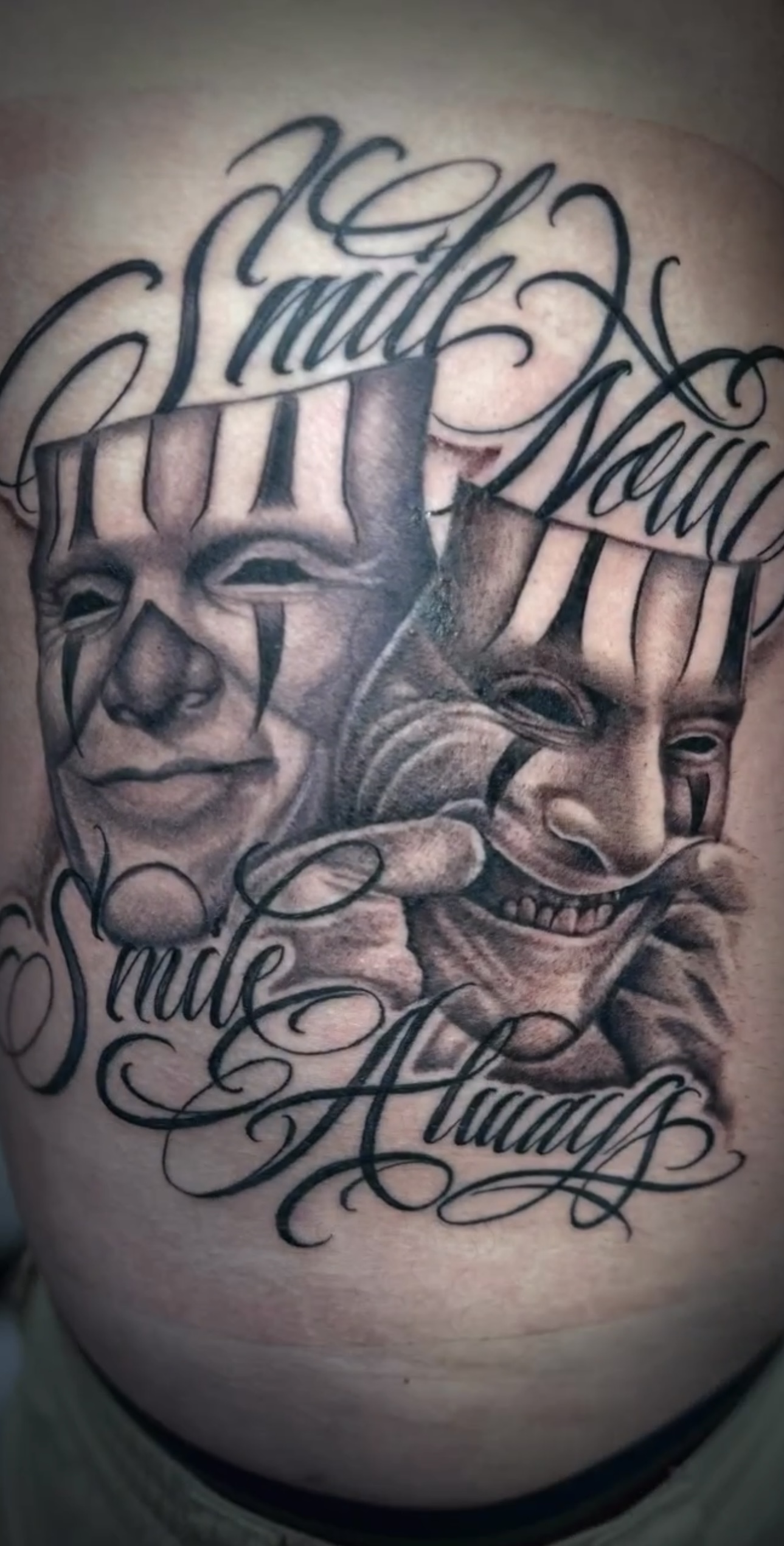 Tattoo featuring two clown faces with intricate shading, accompanied by the phrase "Smile Now, Cry Always," showcasing Alex's artistic style and skill in tattoo artistry.