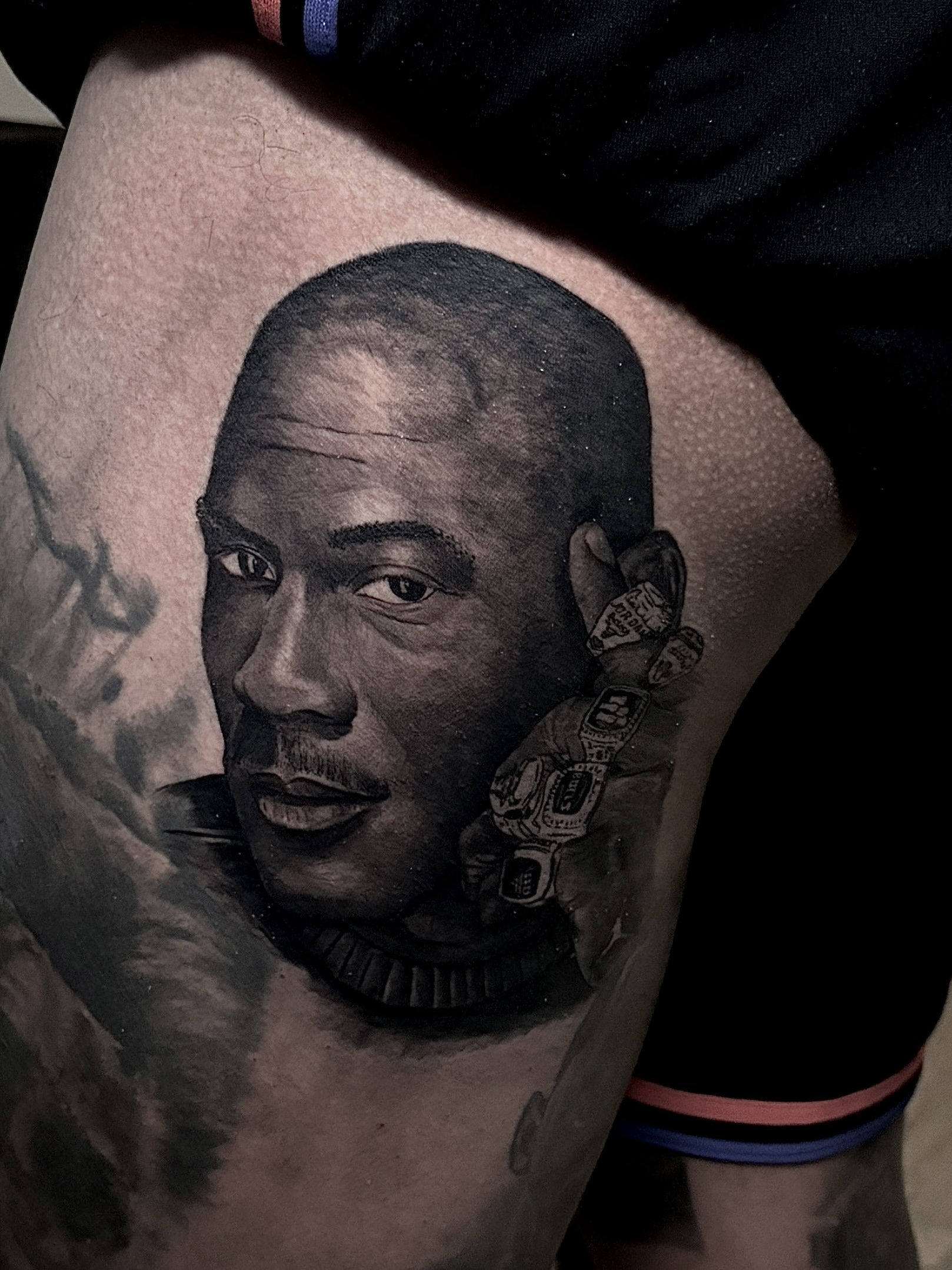 Tattoo of a detailed portrait on a thigh, showcasing a man's face with a confident expression, surrounded by intricate shading and designs, reflecting the artistry of Truth at Game Face Tattoo.