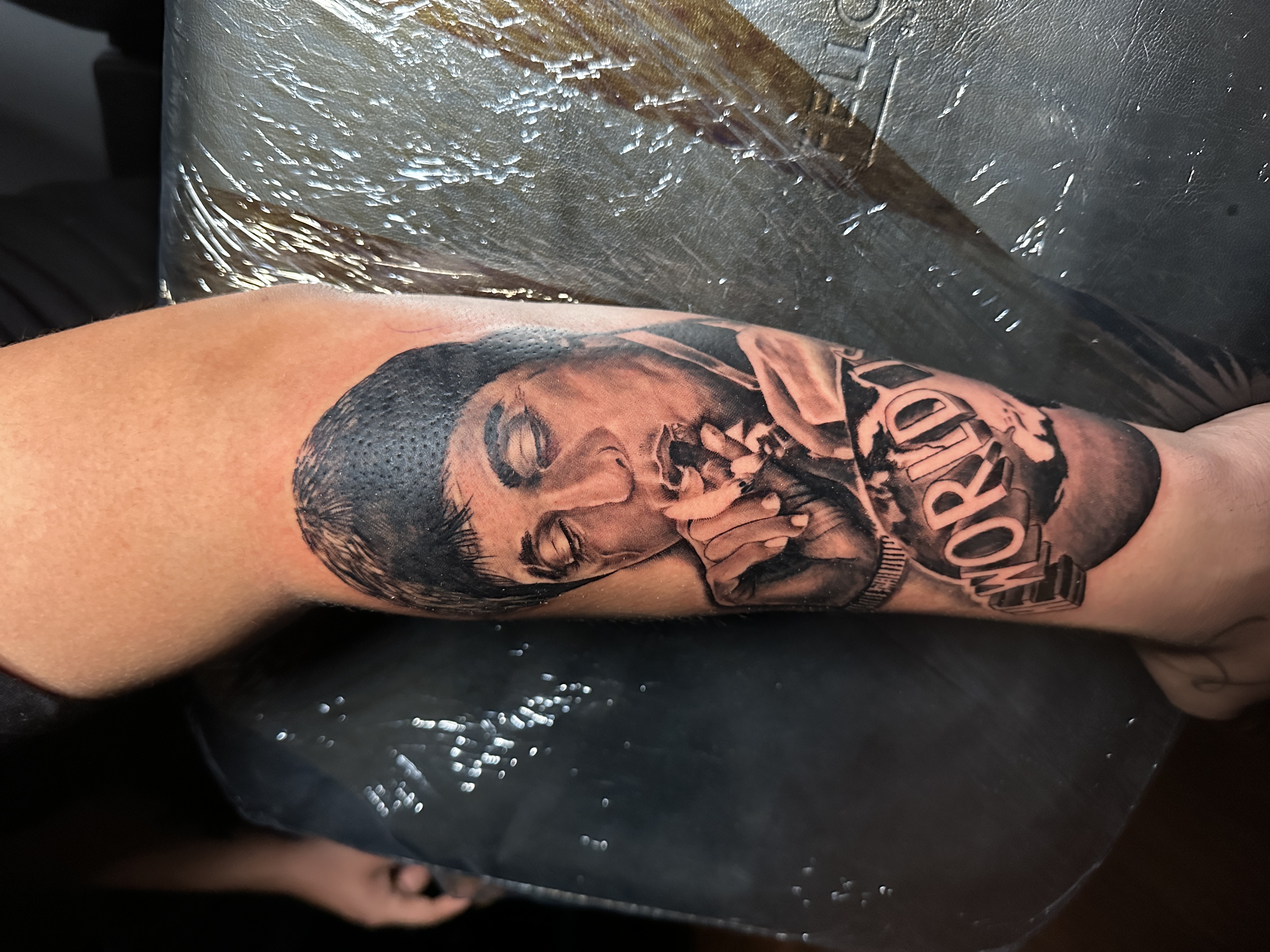 Tattoo of a man with closed eyes and a cigarette, featuring the word "WORLD" prominently, showcasing intricate detail and artistry in a tattoo studio setting.