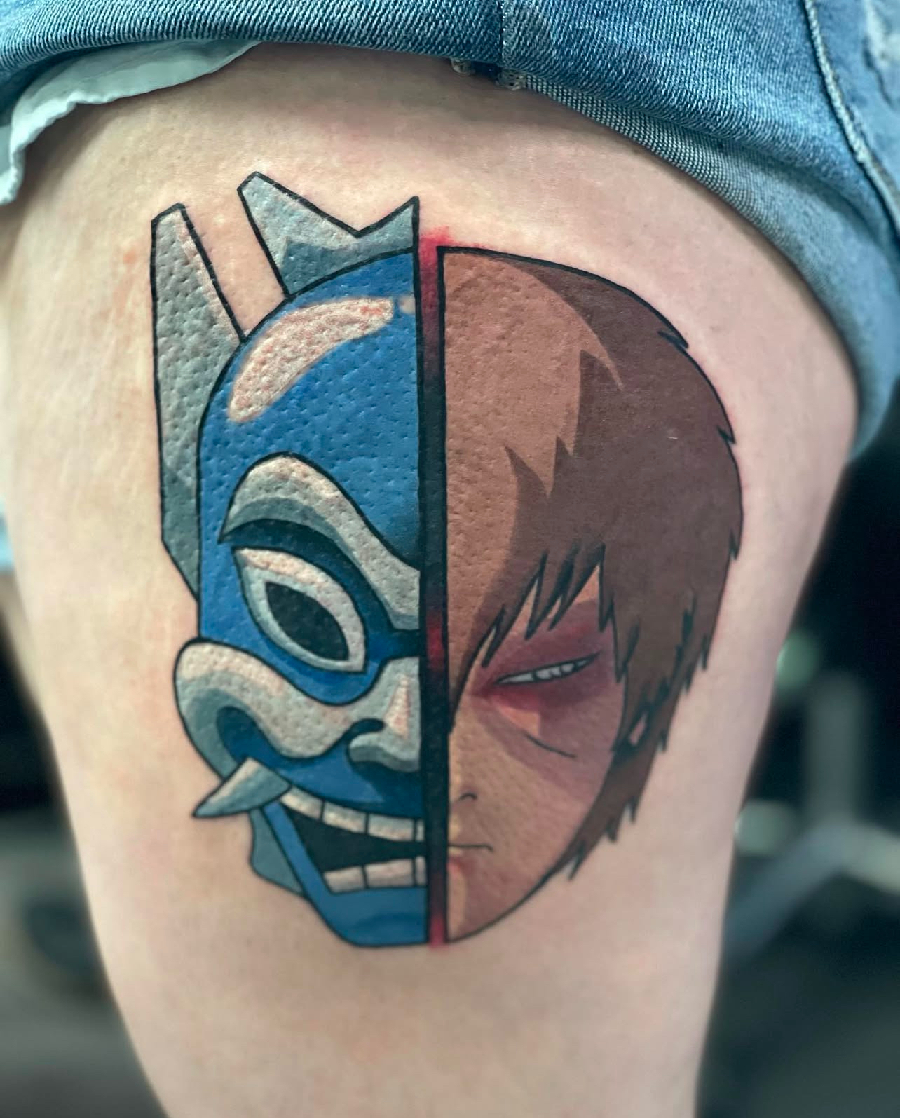 Tattoo design featuring a split face: one side a blue, stylized mask and the other a detailed, serious character portrait, showcasing Edward Madera's artistry at GameFace Tattoo.
