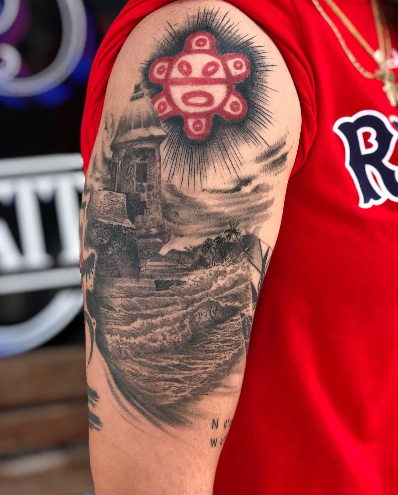 Tattoo on arm featuring a detailed landscape with waves and a tower, highlighted by a red and blue stylized sun symbol, showcasing Edward Madera's artistry at GameFace Tattoo.