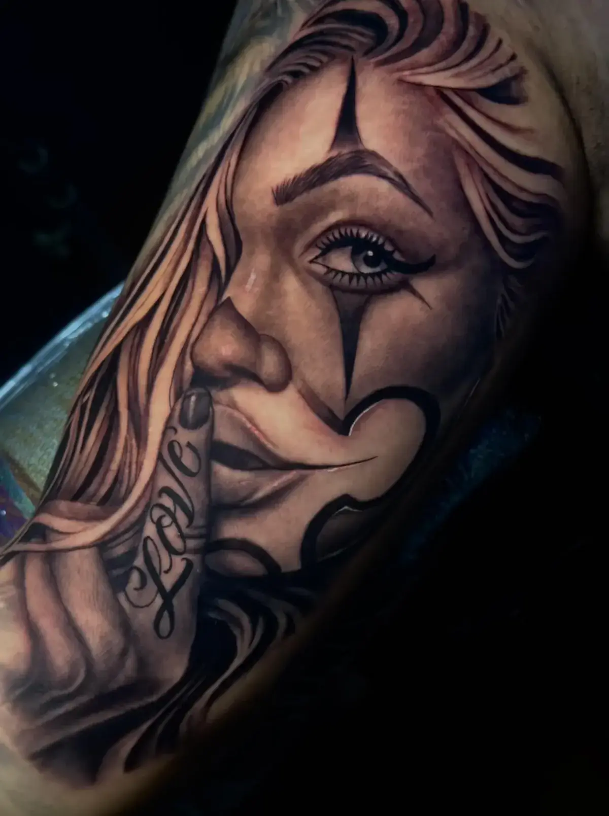 Tattoo of a woman's face with a finger to her lips, featuring intricate shading and the word "Love" on her hand, showcasing artistry and detail in tattoo design at Game Face Tattoo in Orlando, FL.