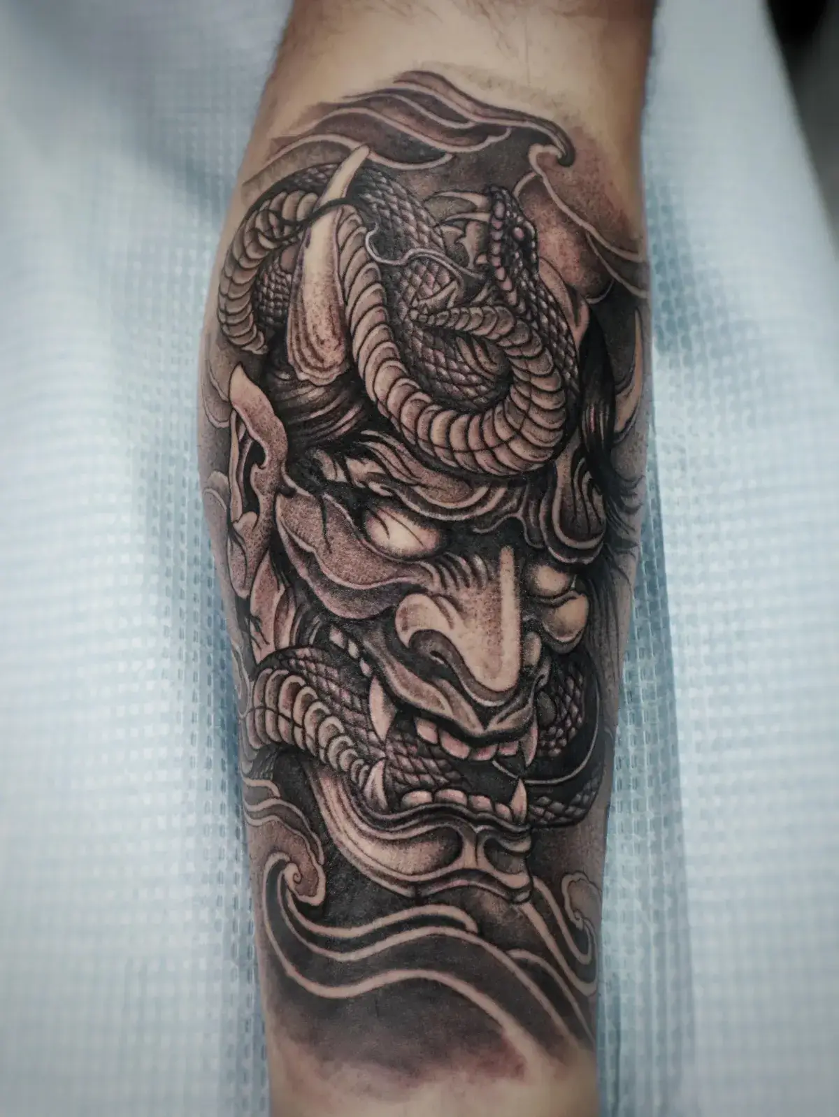 Japanese-style tattoo featuring a fierce demon face intertwined with a serpent, showcasing intricate shading and detail, representing the artistry and craftsmanship of Game Face Tattoo in Orlando, FL.