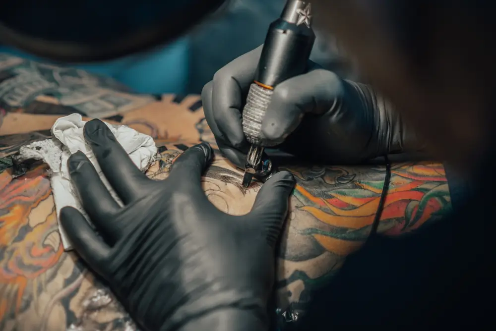 Tattoo artist using a tattoo machine on colorful body art, showcasing intricate designs and creative expression at GameFace Tattoos studio.