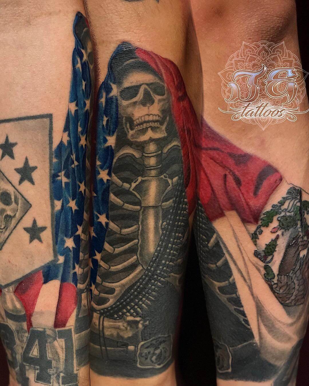 Tattoo design featuring a skeleton adorned with sunglasses, draped in an American flag, showcasing intricate black and grey shading, alongside additional tattoo elements like a skull and floral patterns.