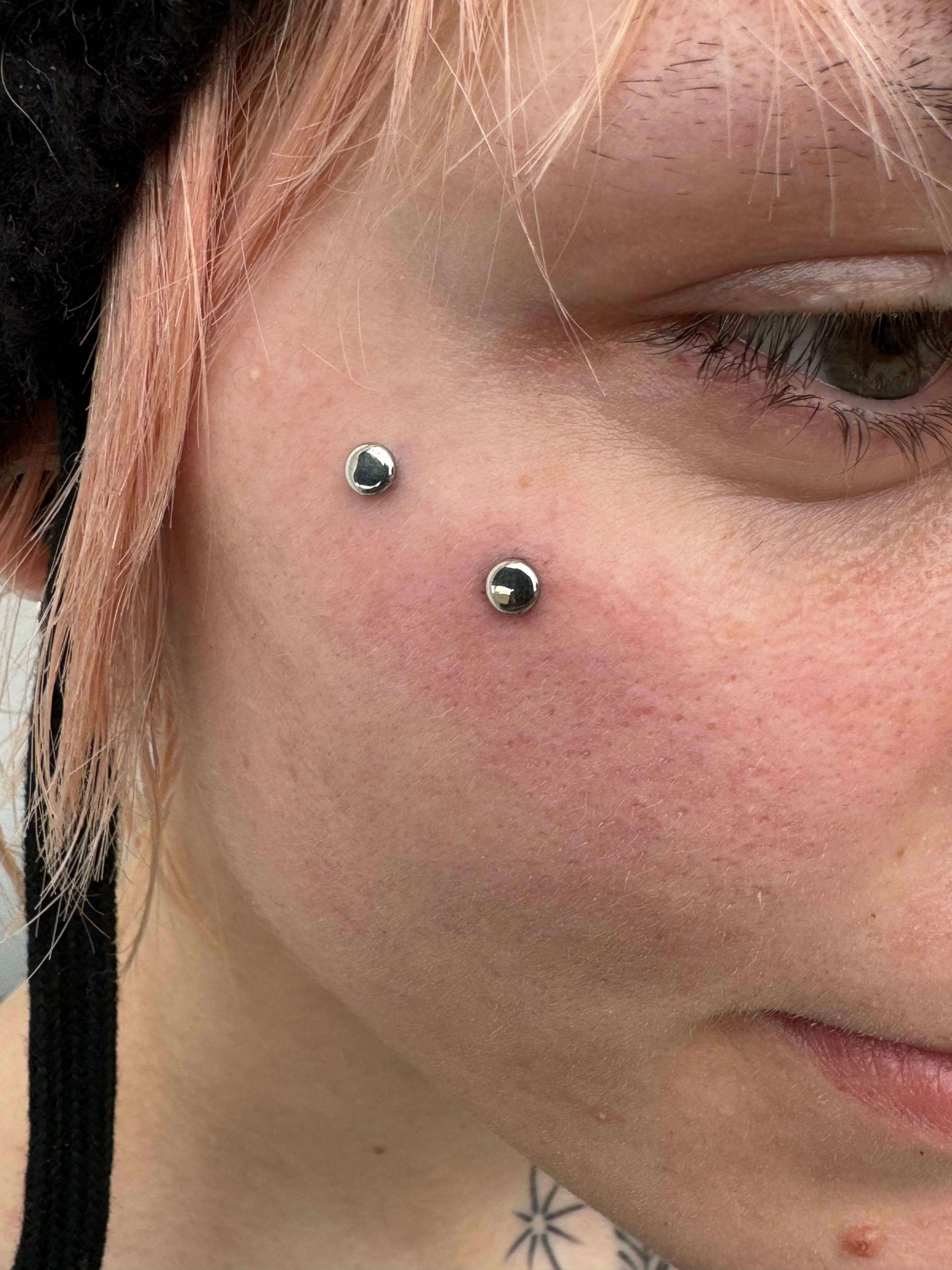 Facial piercings featuring two microdermal implants on the cheek, showcasing a stylish body modification look.