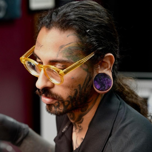 Tattoo artist with a beard and tattoos, wearing a cap, showcasing expertise and artistry in body art at GameFace Tattoos.