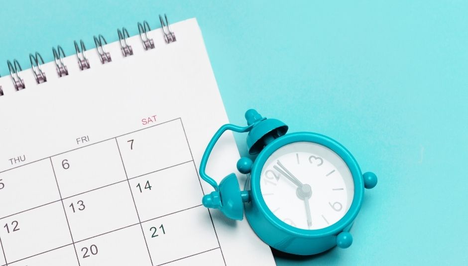 Calendario da tavolo con spirale e piccola sveglia turchese su sfondo azzurro, simbolo di come ottimizzare tempo e produttività nel business.