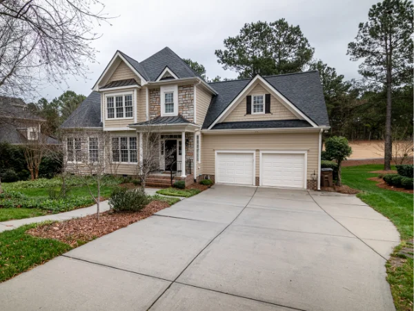 A large two-story house with beige siding, stone facade, and a two-car garage, viewed from the driveway.