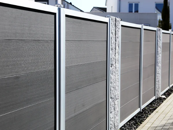 A close-up view of a modern garden privacy fence with dark grey panels and decorative stone posts.