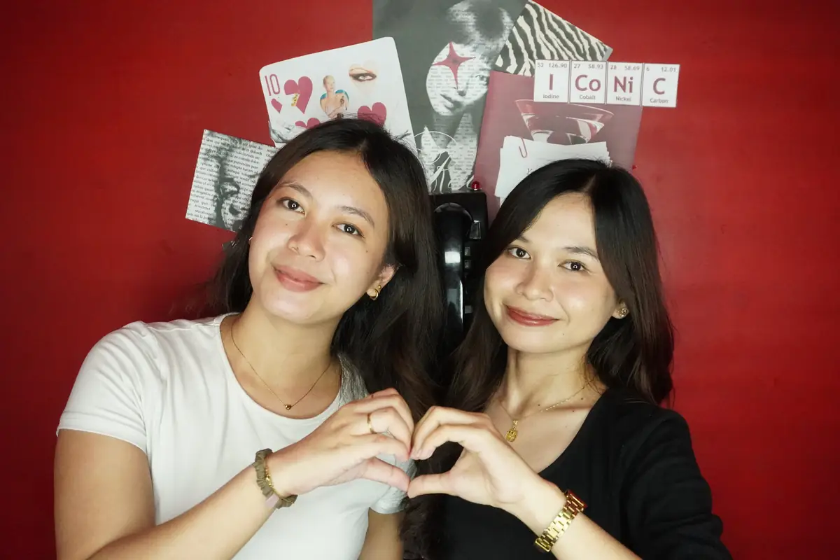 Two friends making a heart against the red wall at Big House
