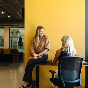 Two professional women in mentoring conversation, focused and supportive interaction, leadership development setting