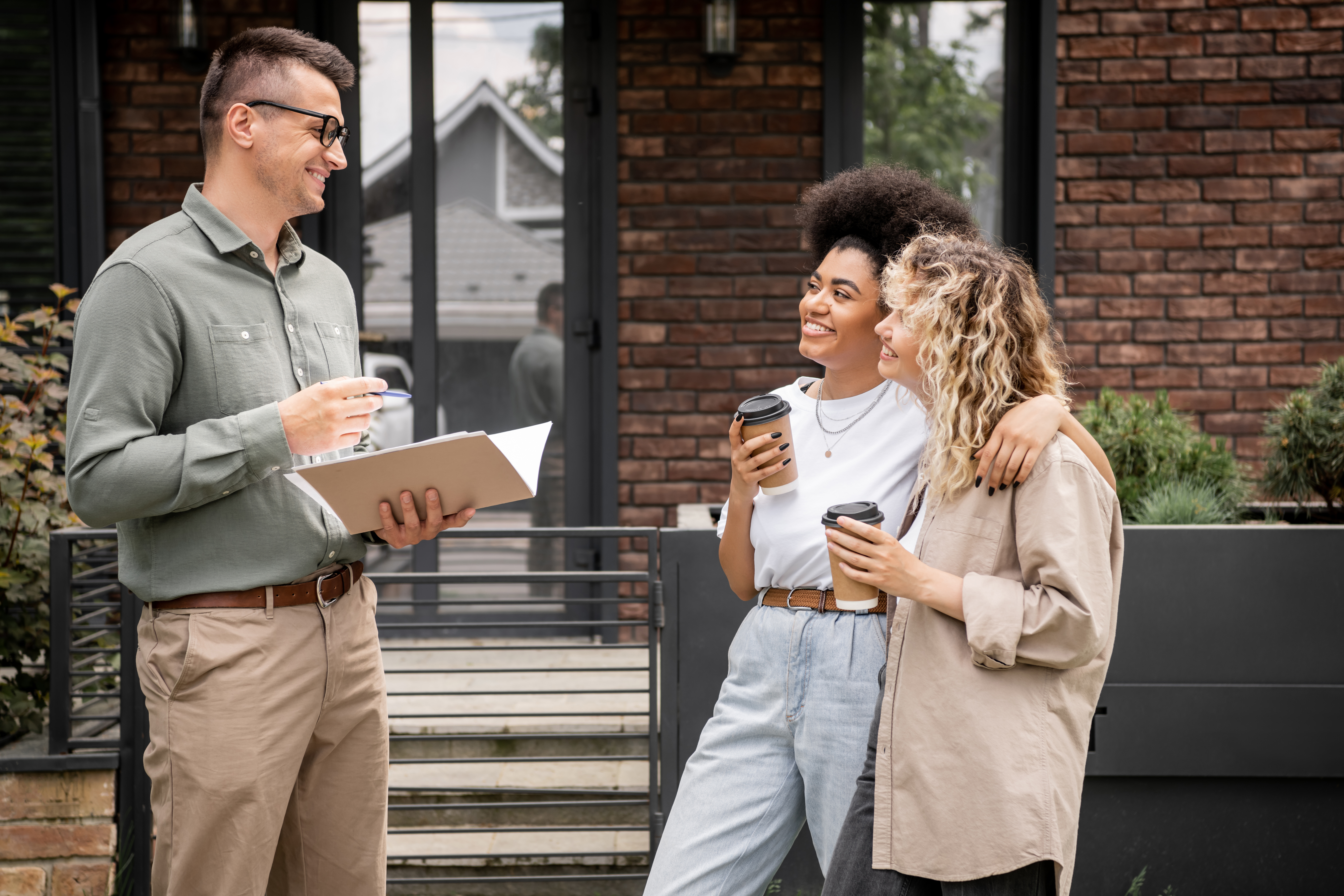 real estate agent meeting with past clients over coffee or having a friendly conversation outside a home.