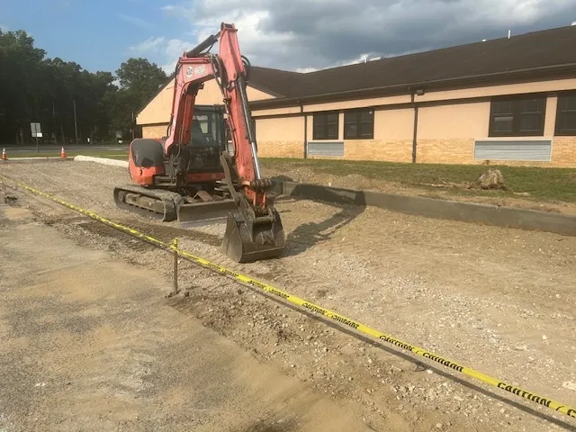 Partially constructed or unrenovated railroad industrial site with a long, narrow concrete trench running through the center. The trench is bordered by raised concrete edges, and the surrounding area appears to be a warehouse or a similar large indoor space. Scaffolding, construction equipment, and safety barriers are visible in the background, indicating ongoing construction or maintenance work.