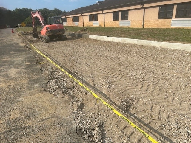 Partially constructed or unrenovated railroad industrial site with a long, narrow concrete trench running through the center. The trench is bordered by raised concrete edges, and the surrounding area appears to be a warehouse or a similar large indoor space. Scaffolding, construction equipment, and safety barriers are visible in the background, indicating ongoing construction or maintenance work.