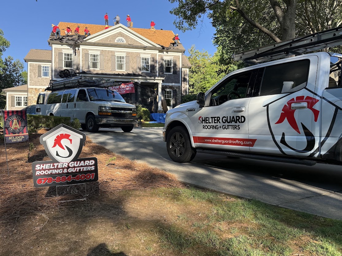 A Shelter Guard Roofing and Gutters crew working on a large house roof, with the company truck, van and yard sign in the foreground.