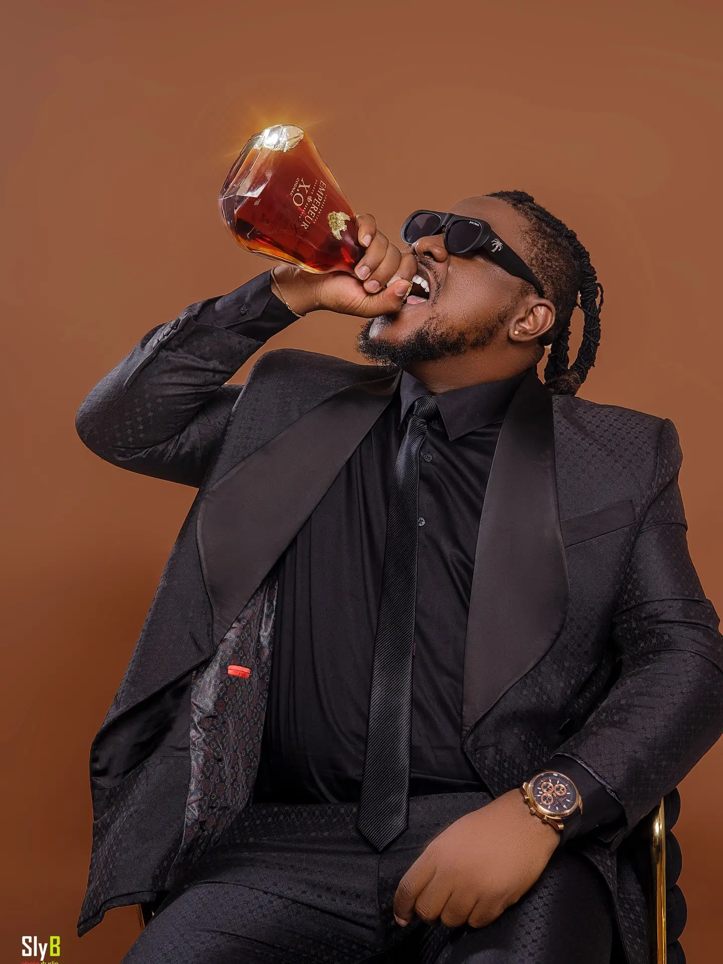 Man in a black suit and sunglasses drinking directly from a cognac bottle.