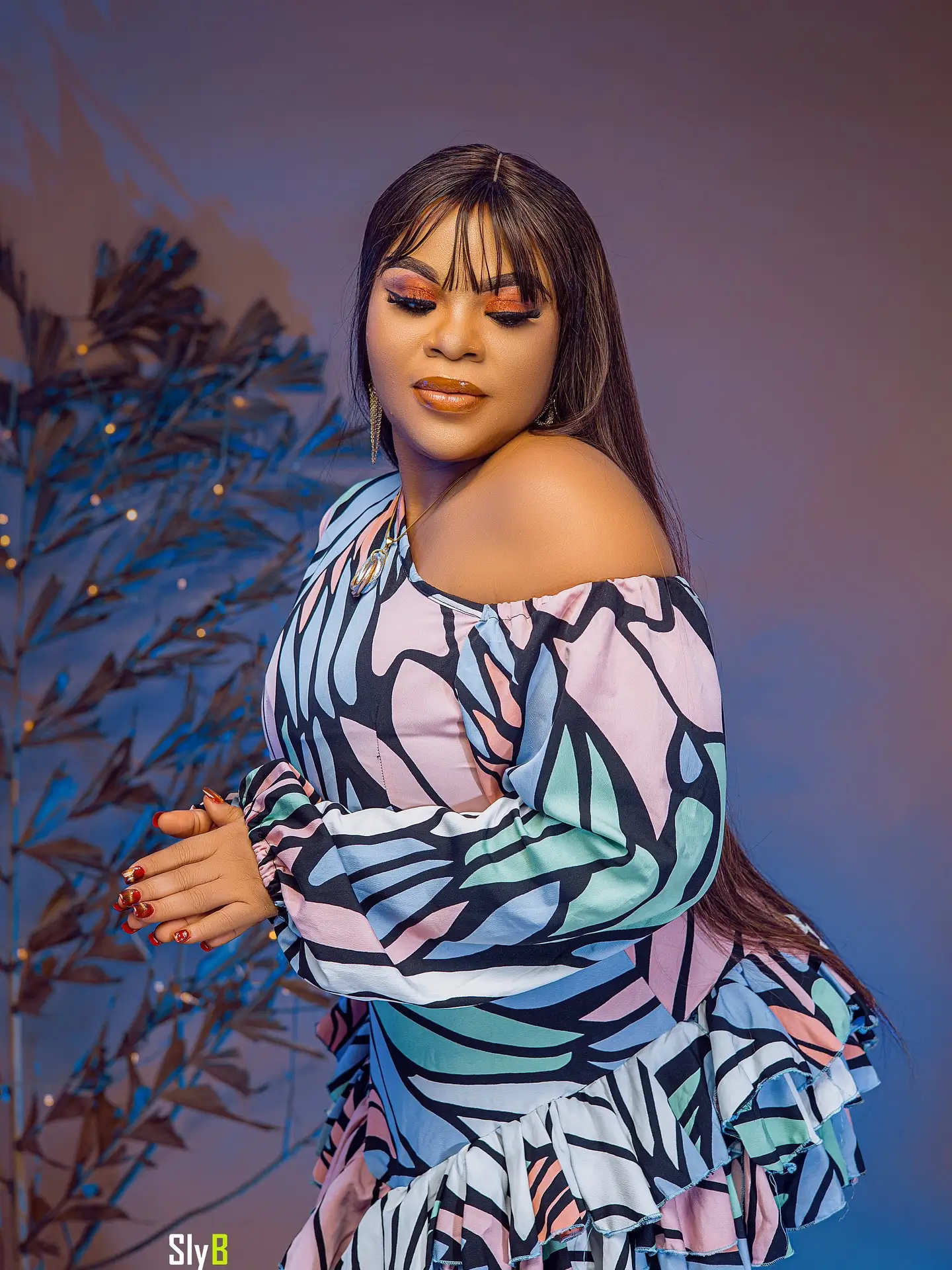 Woman in a colorful off-shoulder dress posing in profile against a blue-lit background.