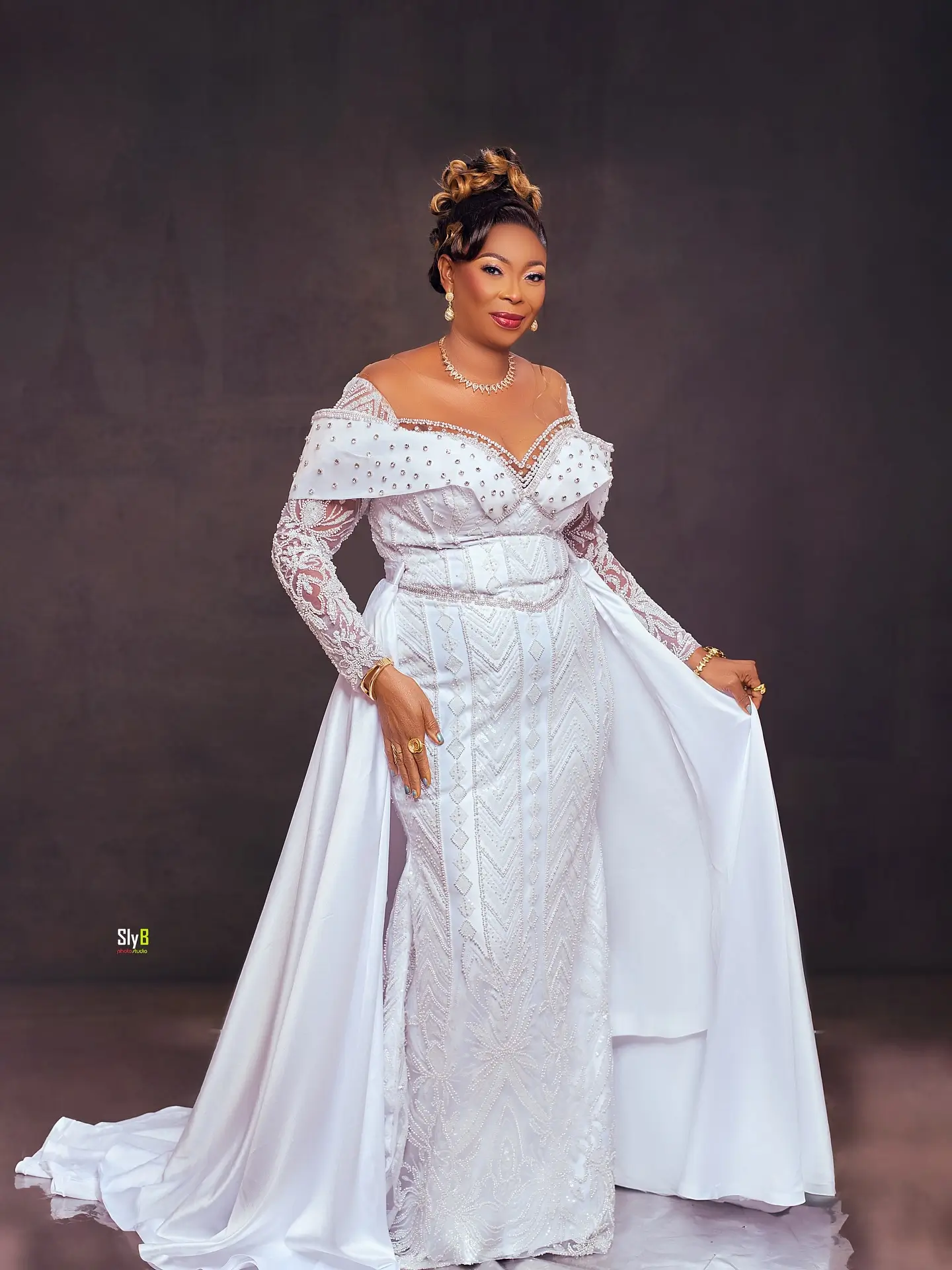 Woman in a white beaded gown smiling while holding the train of her dress.