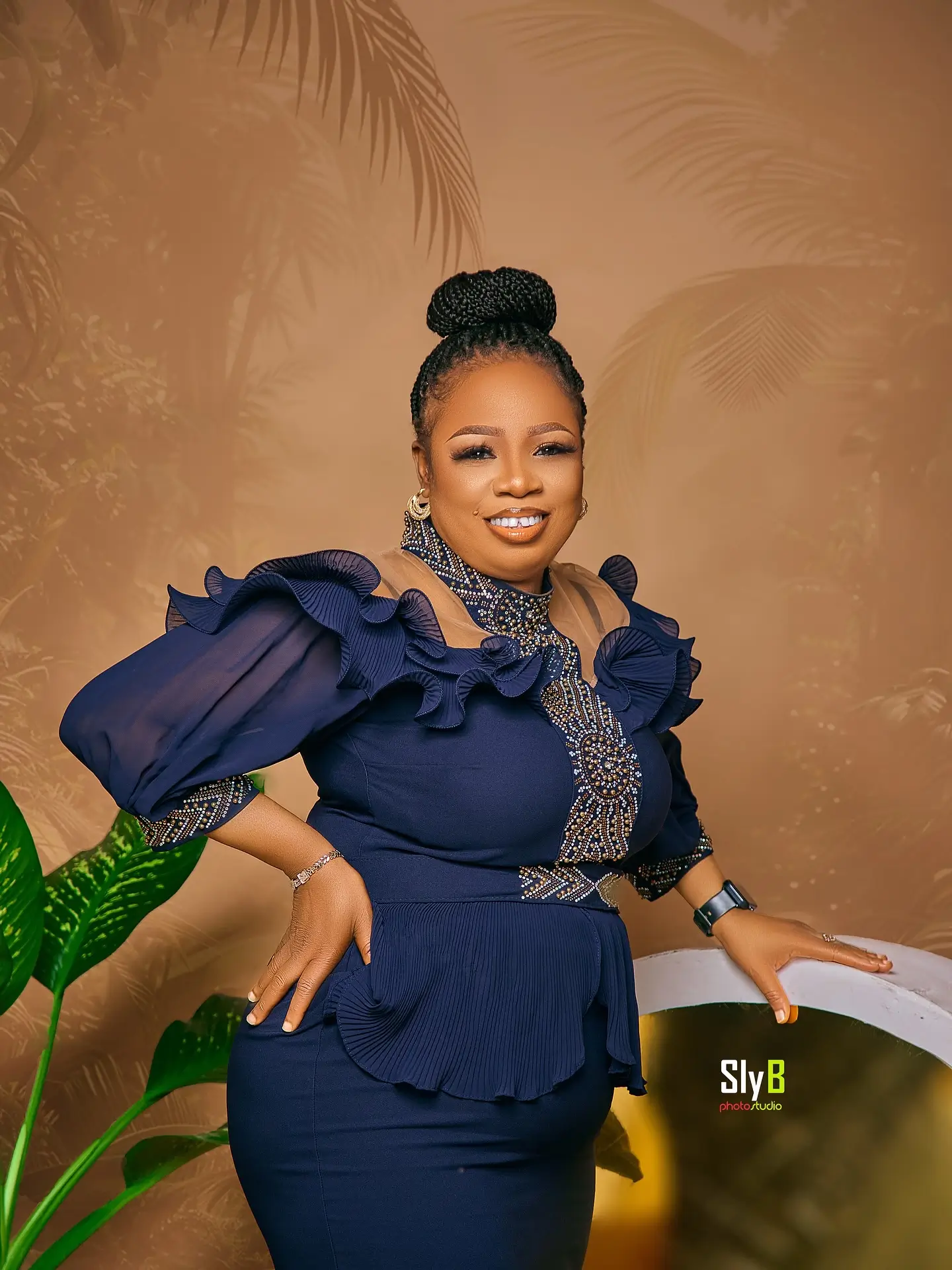Woman in a navy ruffled top with beaded detail standing near a palm-patterned backdrop.