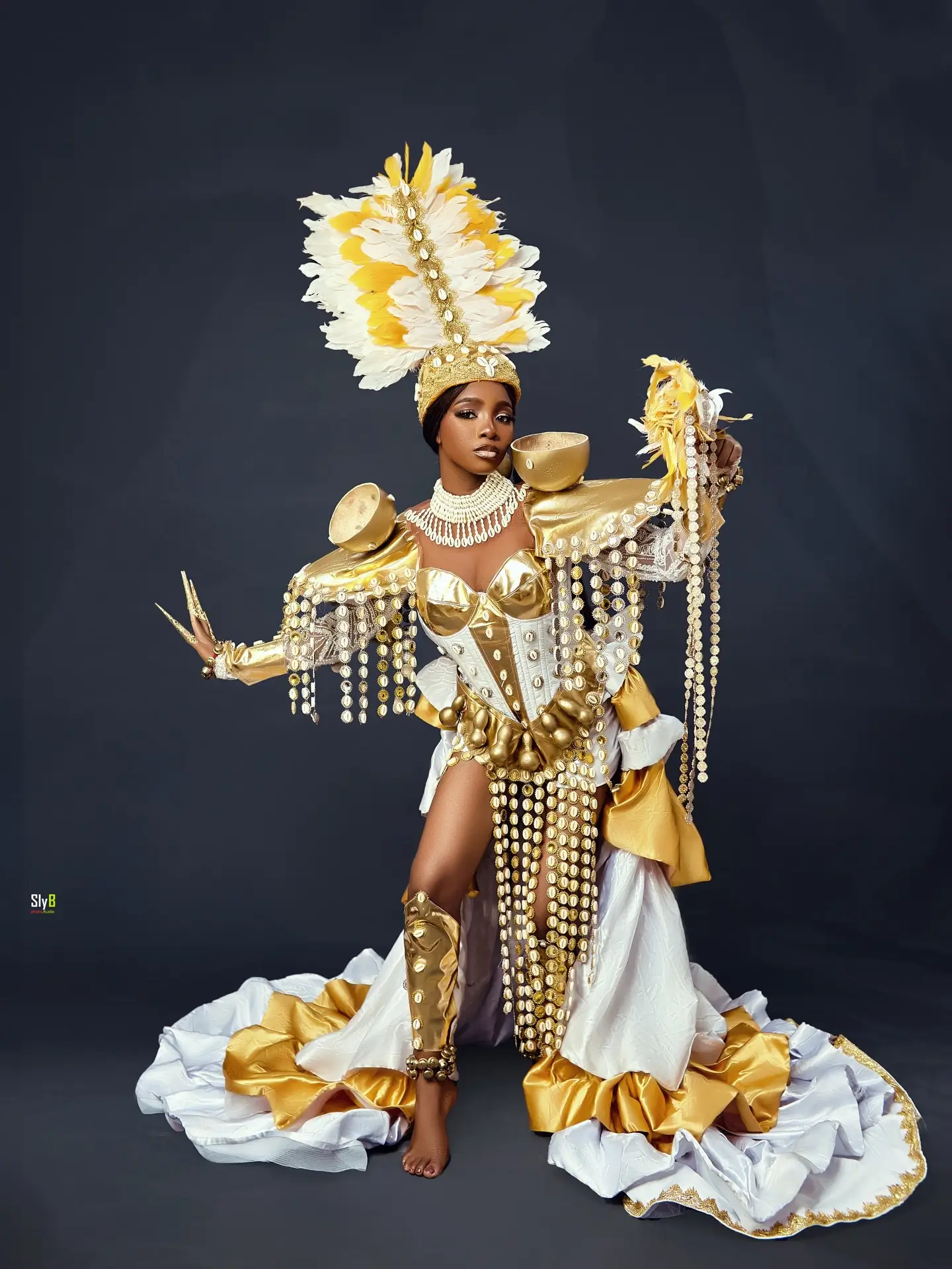 Woman in a gold and white feathered costume posing with her arms extended.