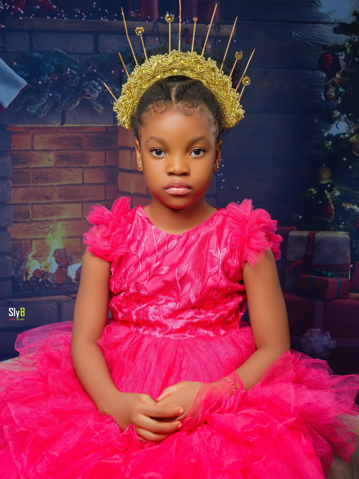 Close-up portrait of a girl in a pink dress wearing a gold spiked crown.