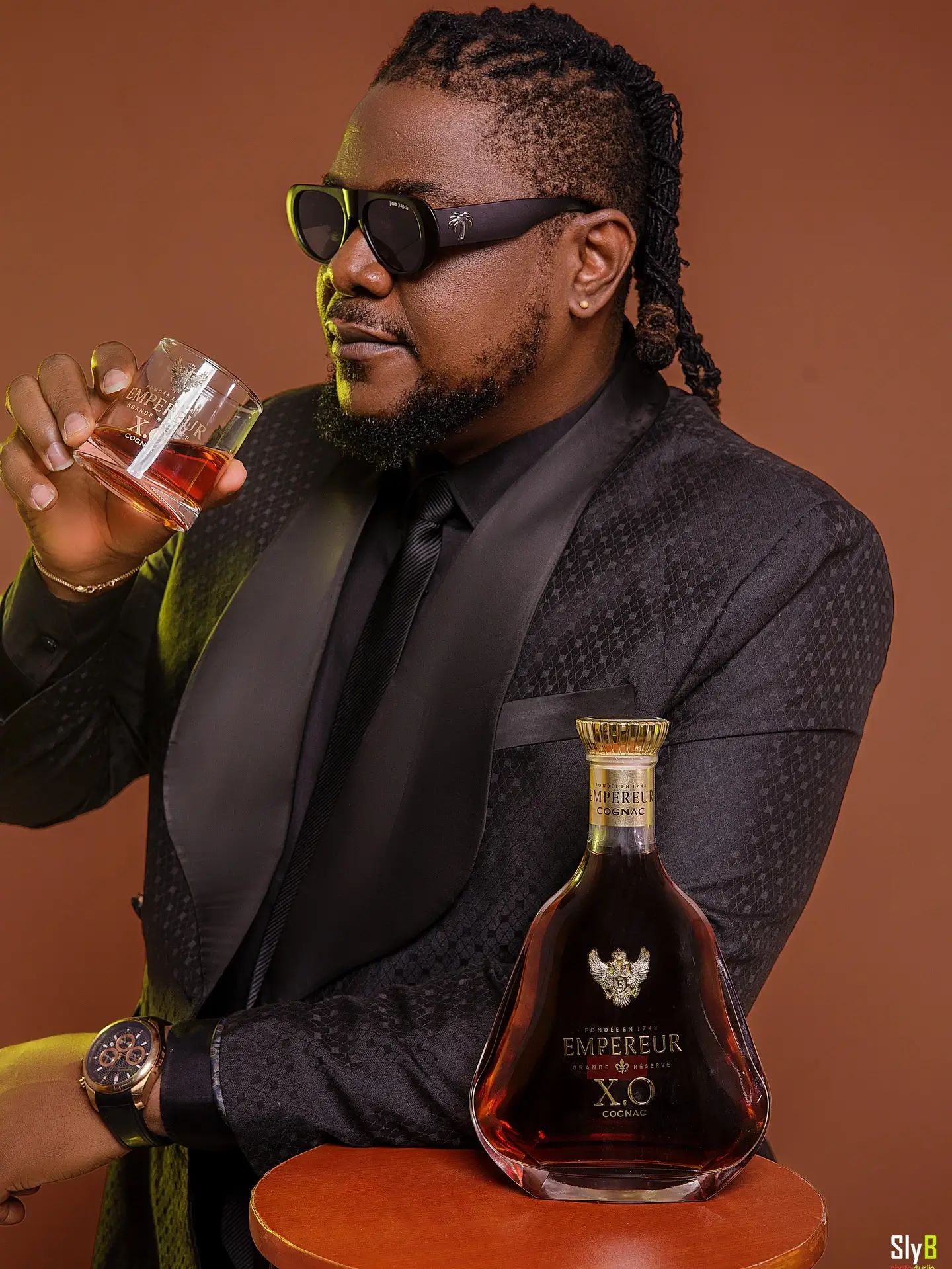 Man in a black suit holding a glass of cognac beside a bottle of Empereur XO.