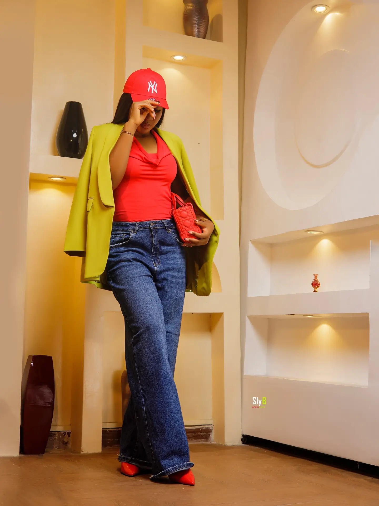 Woman in a lime green blazer and red baseball cap holding a red handbag.