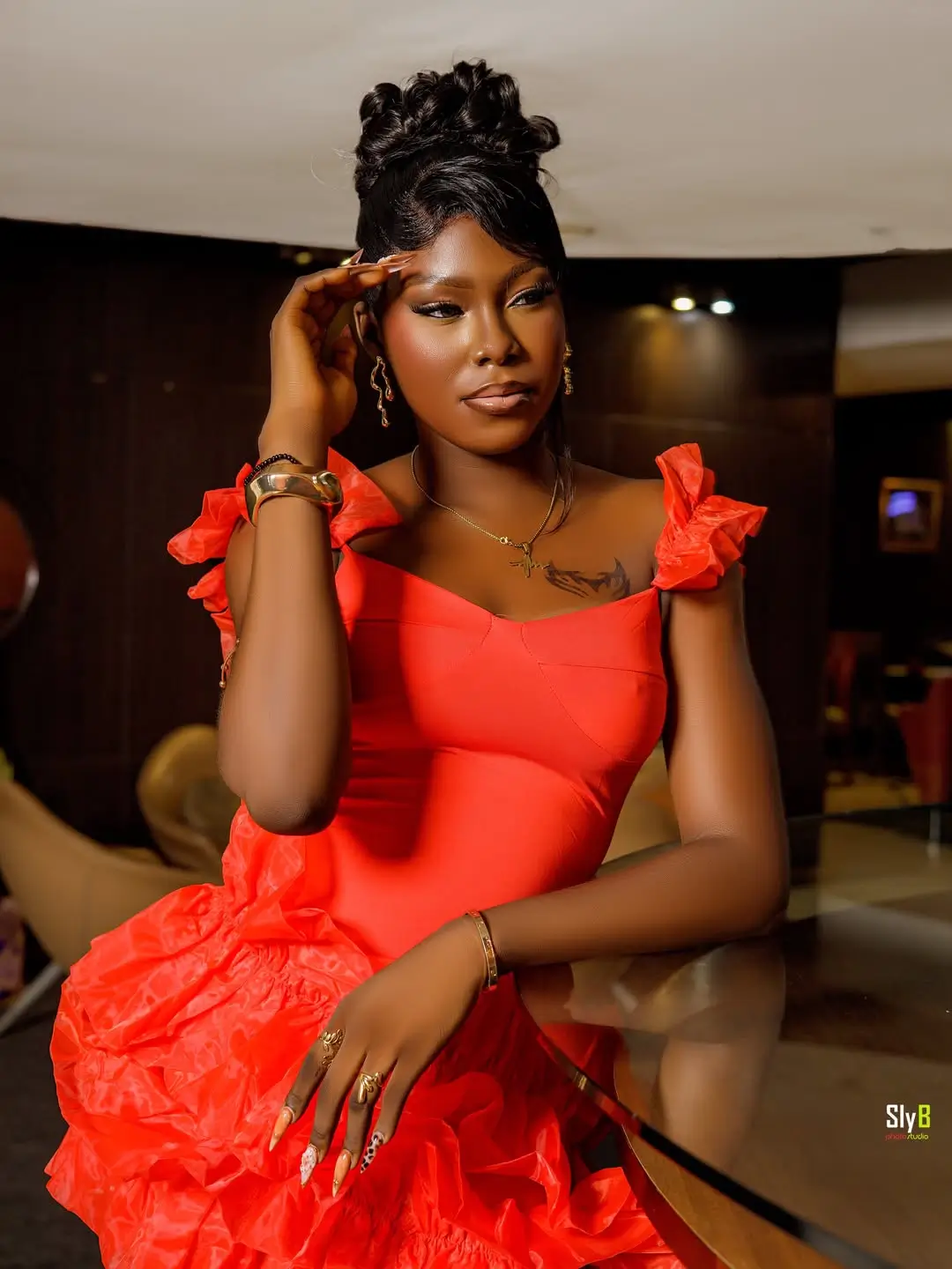 Woman in an orange ruffled dress seated at a glass table in a lounge.