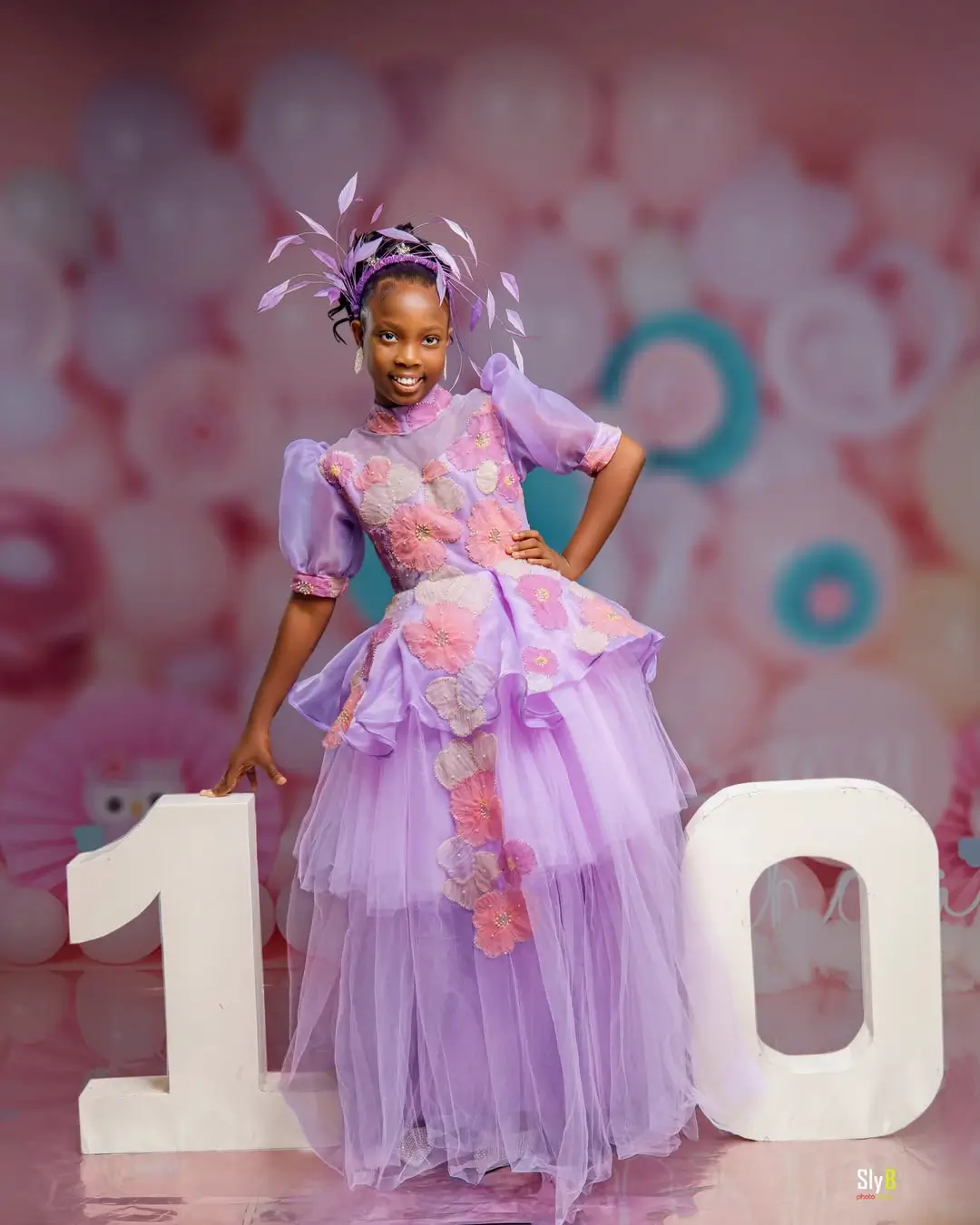 Girl in a purple floral dress posing beside number ten decorations for her birthday.