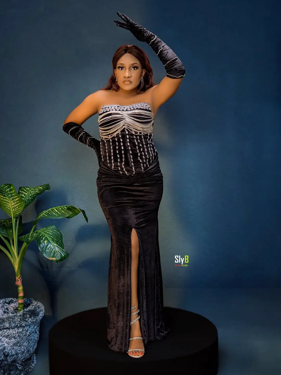 Woman in a black beaded velvet gown and long gloves posing with her hand raised.