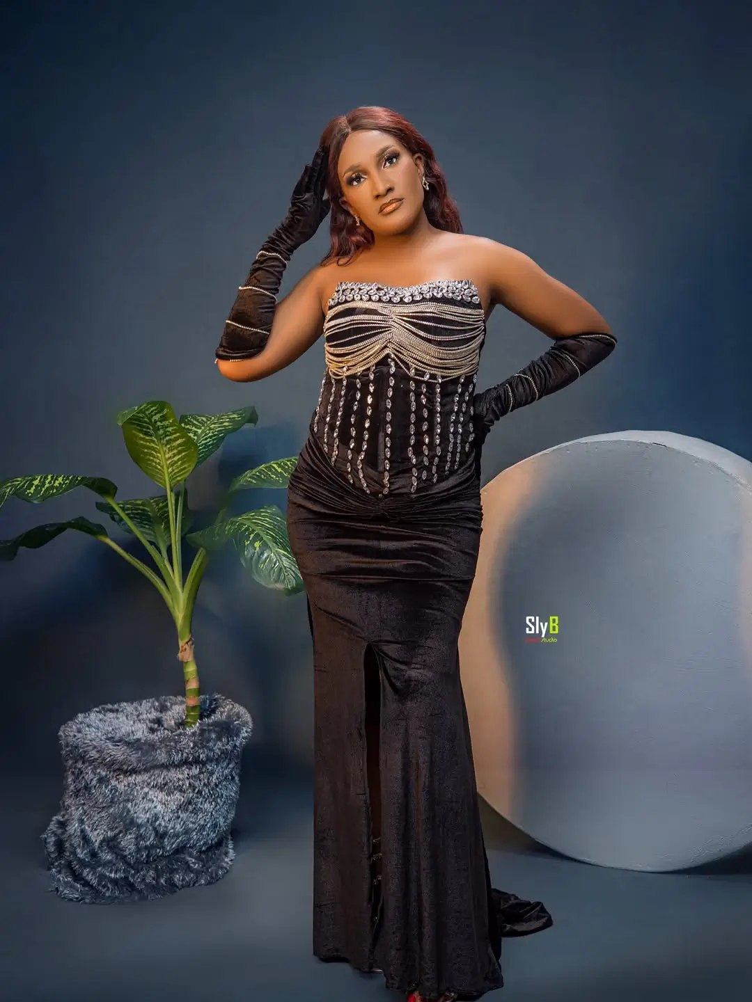 Woman in a black beaded velvet gown and gloves standing with her hand on her hip.