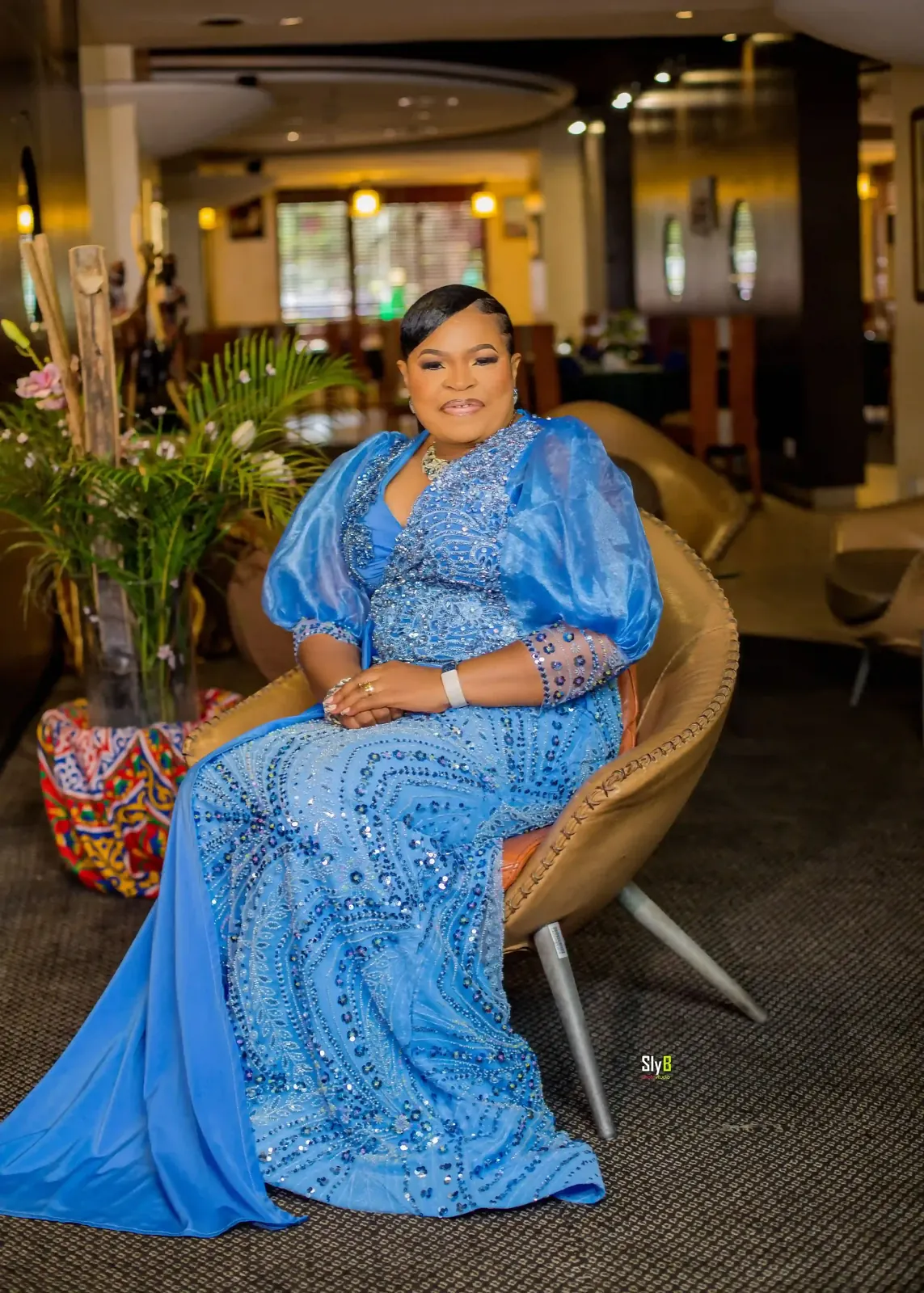 Woman seated indoors wearing a blue floor-length formal gown