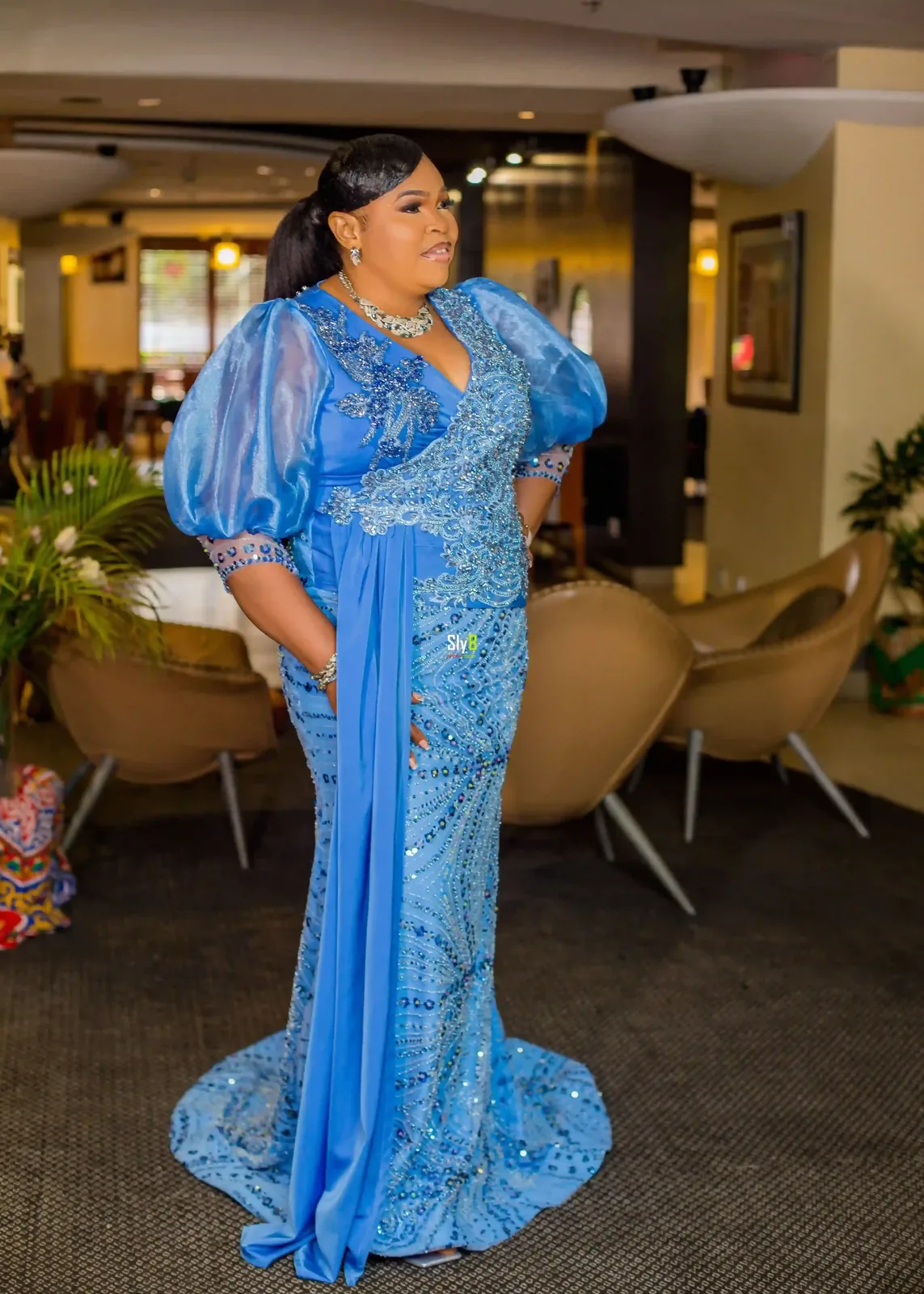 Woman standing indoors in a blue floor-length formal gown