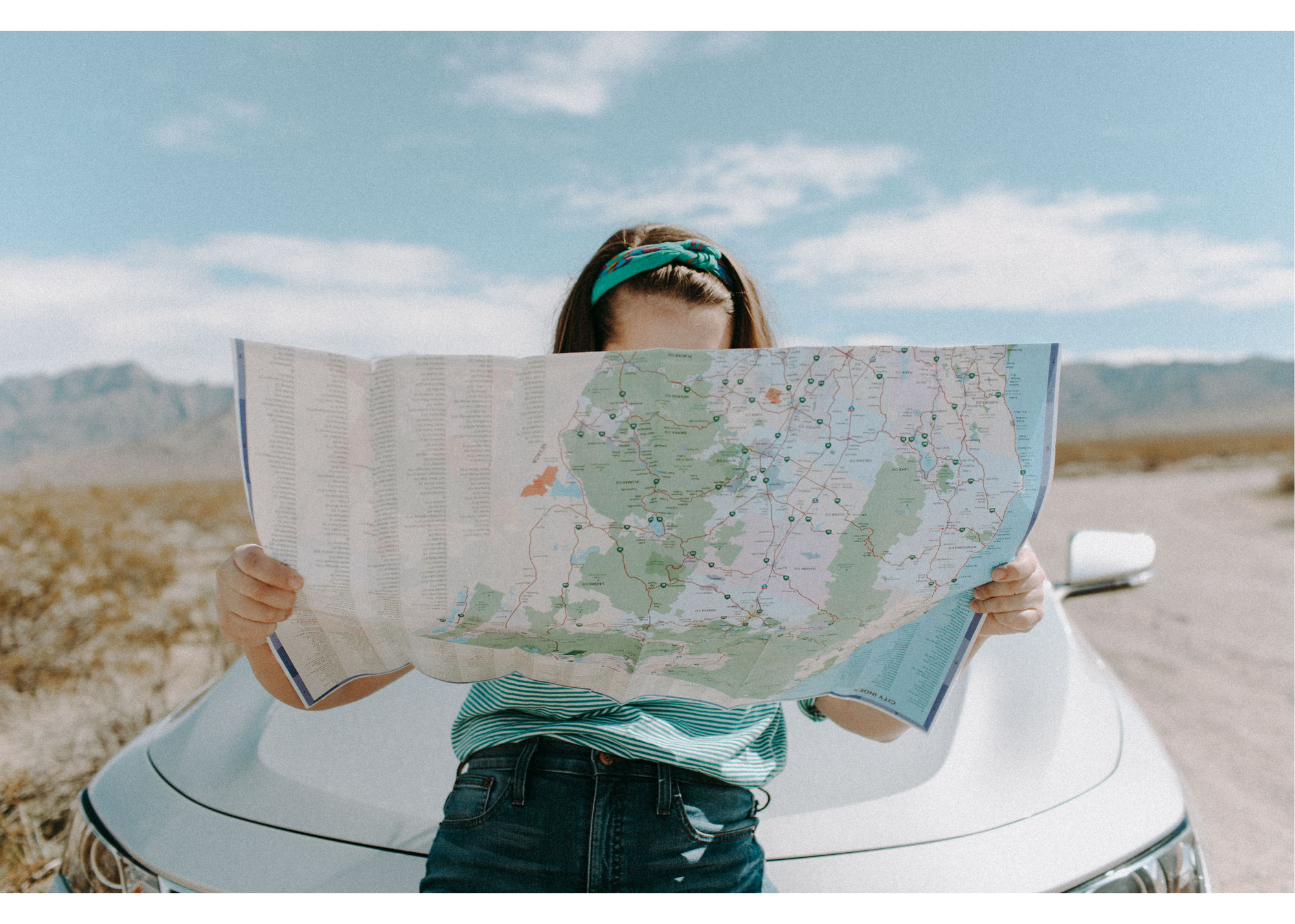 A woman looking at a map sitting on the bonnet of a car