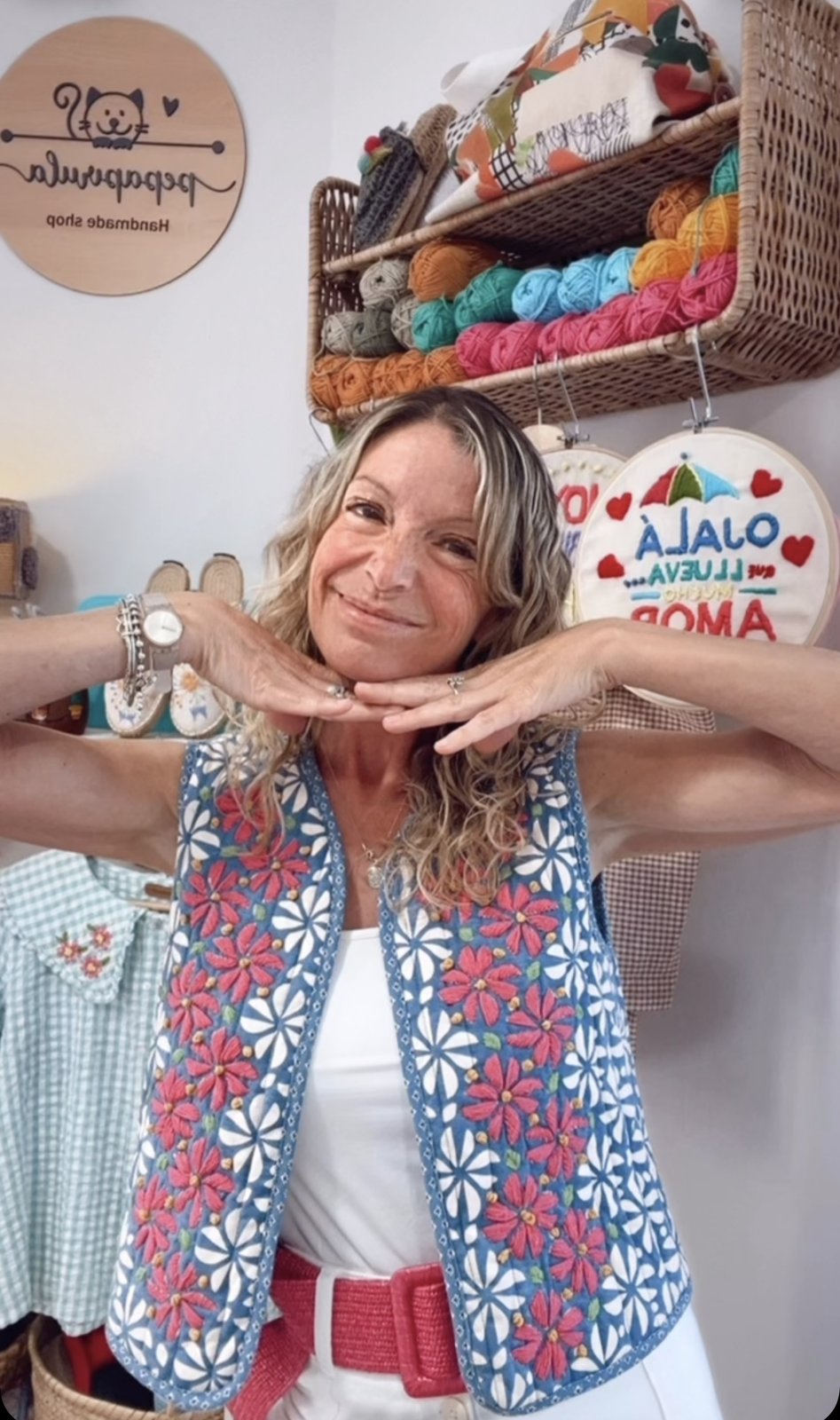 Trini sonriendo con las manos en las mejillas entre sus lanas y sus bastidores