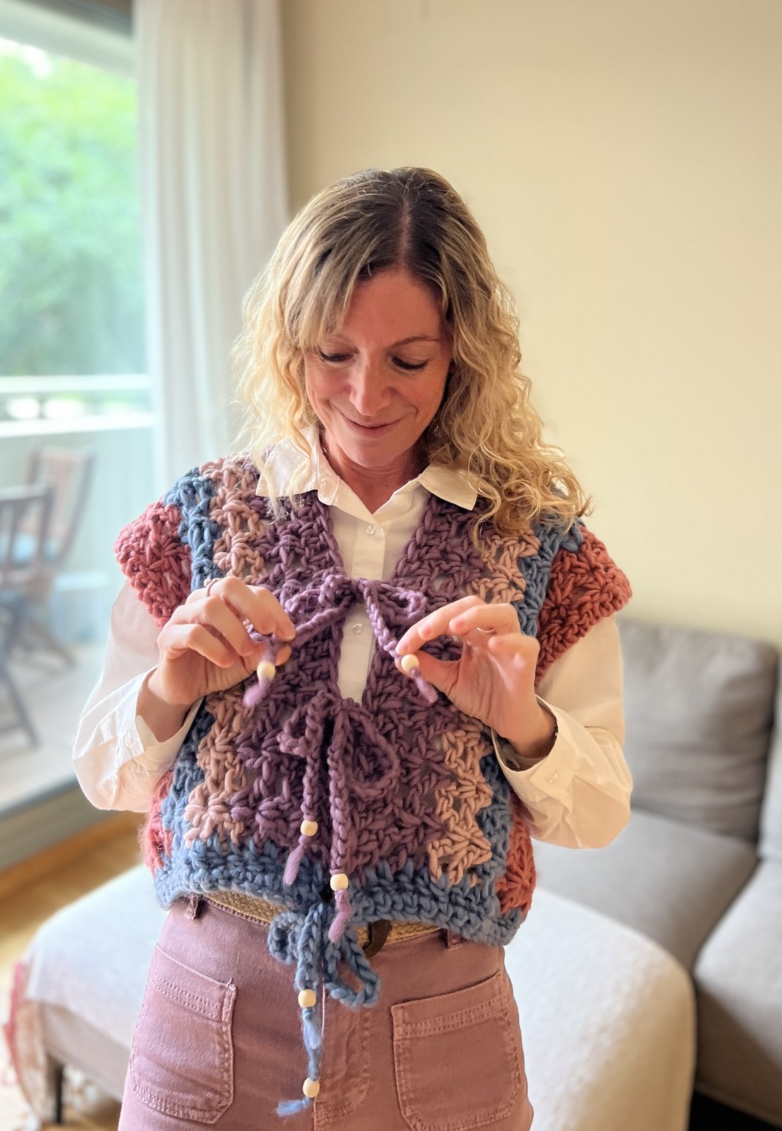 Trini sonriendo mientras anuda con sus manos un chaleco de crochet lila