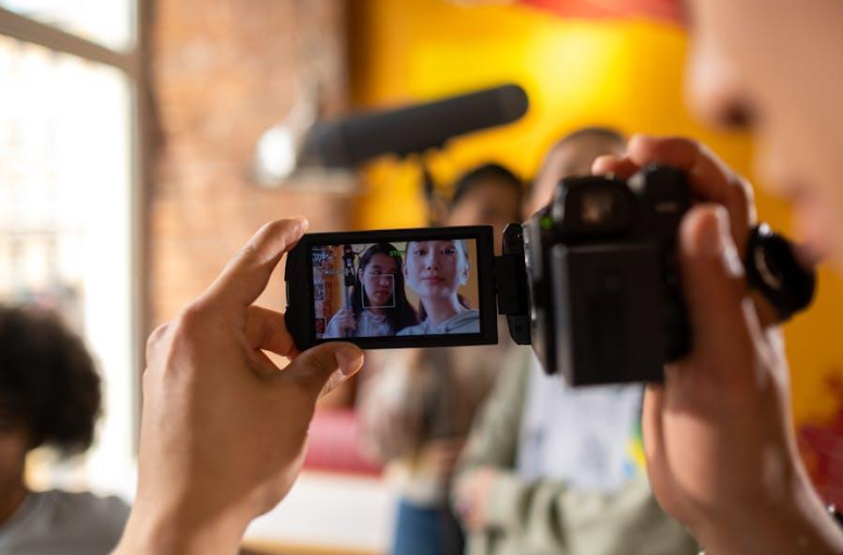 Person filming two people on camera during a video recording.