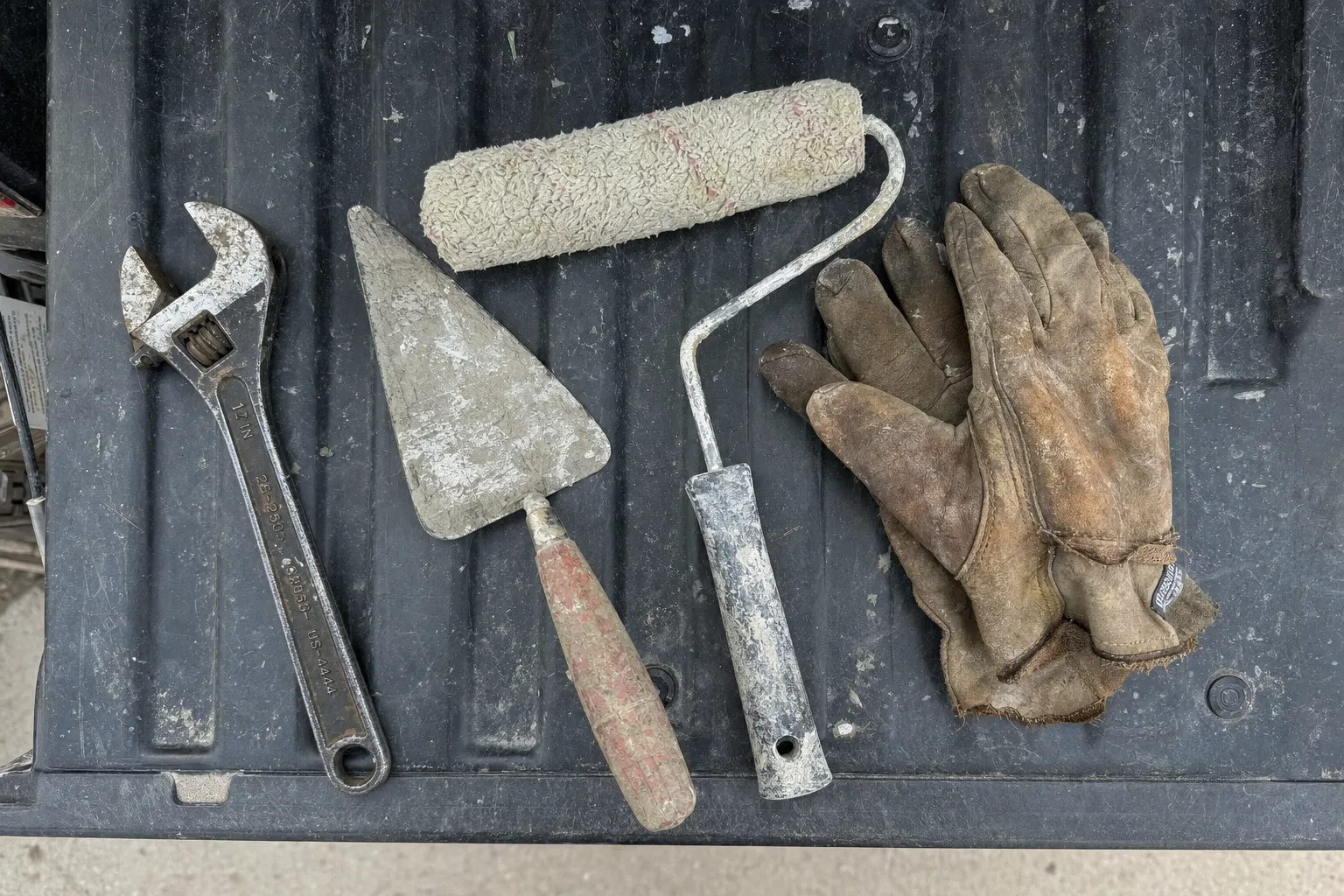 A flat-lay of home service tools from a few different trades (a wrench, a paint roller, a small trowel, work gloves) arranged naturally on a truck tailgate or workbench A flat-lay of home service tools from a few different trades (a wrench, a paint roller, a small trowel, work gloves) arranged naturally on a truck tailgate or workbench